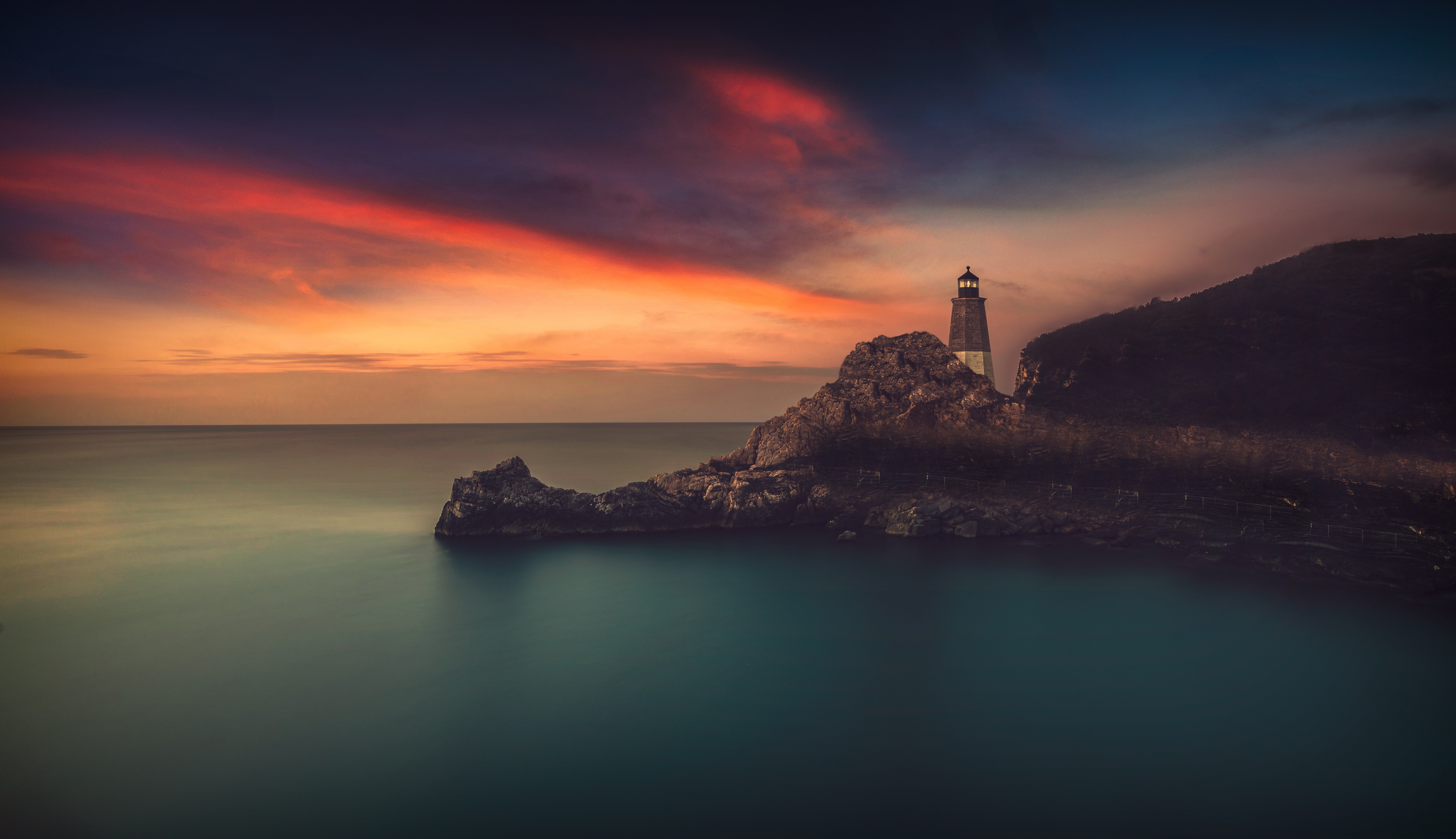Lighthouse on a rocky outcrop at sunset HD Wallpaper