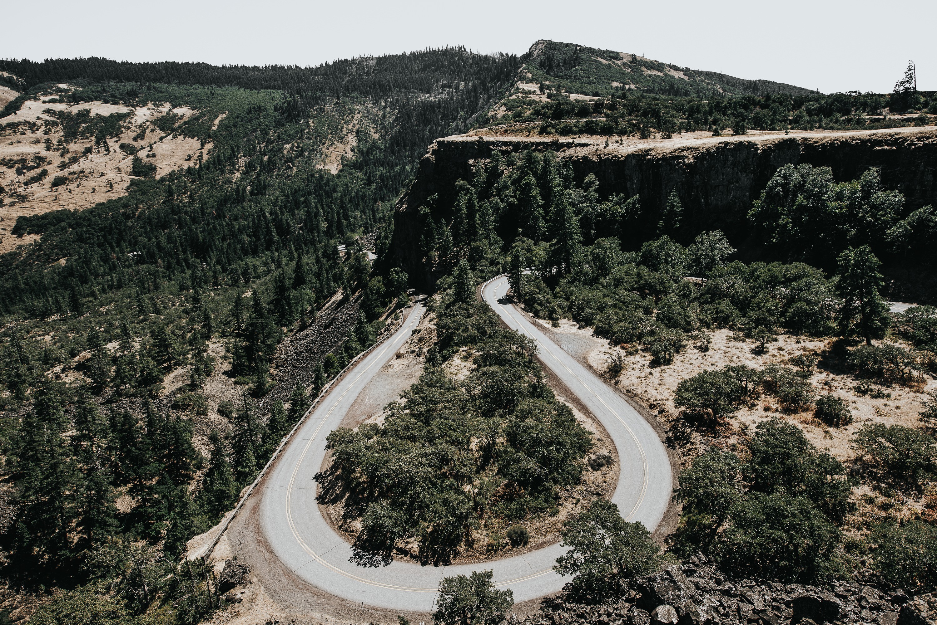Winding mountain road through a forested landscape HD Wallpaper
