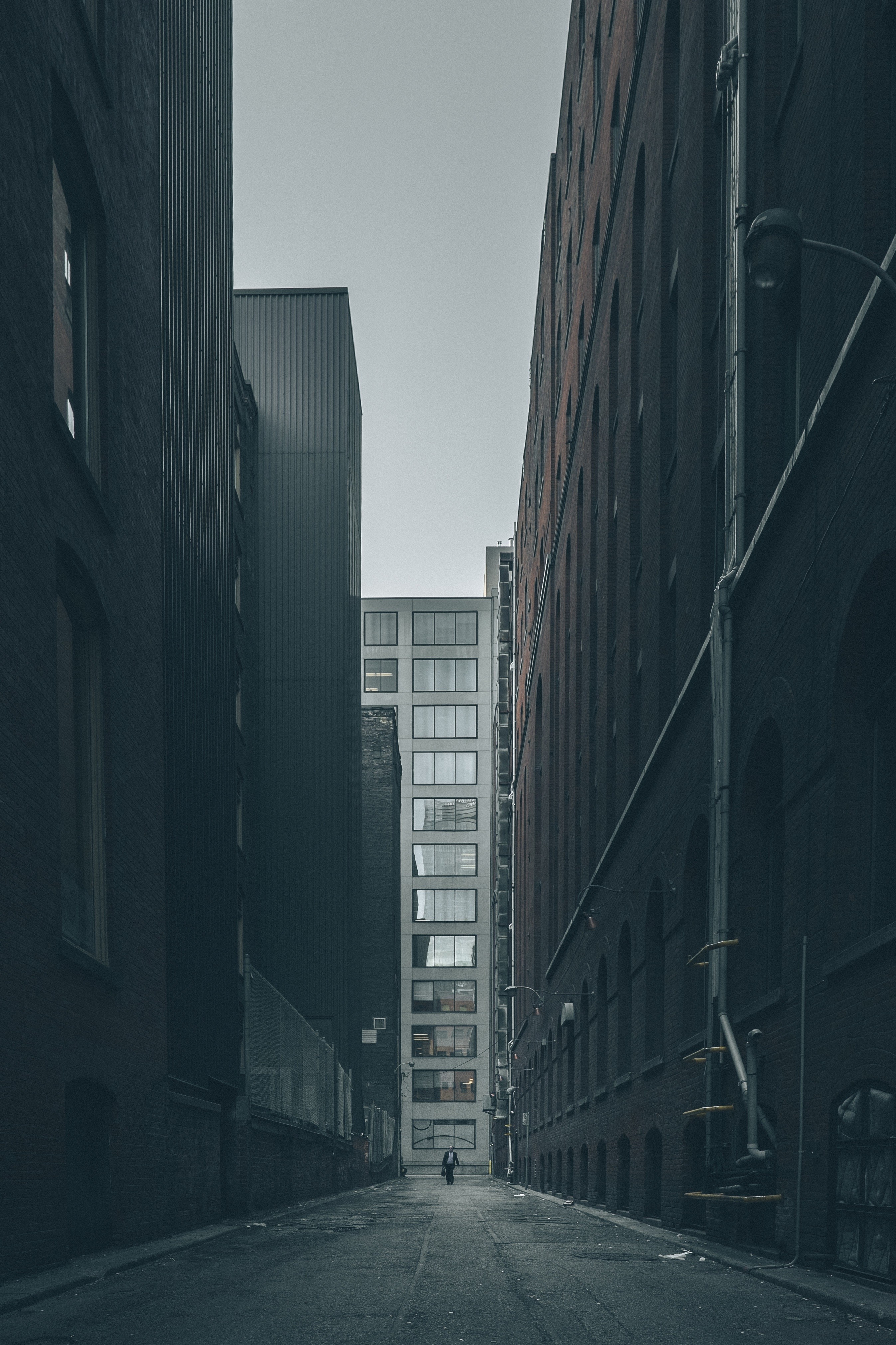 Man walks down a narrow alley between tall buildings HD Wallpaper