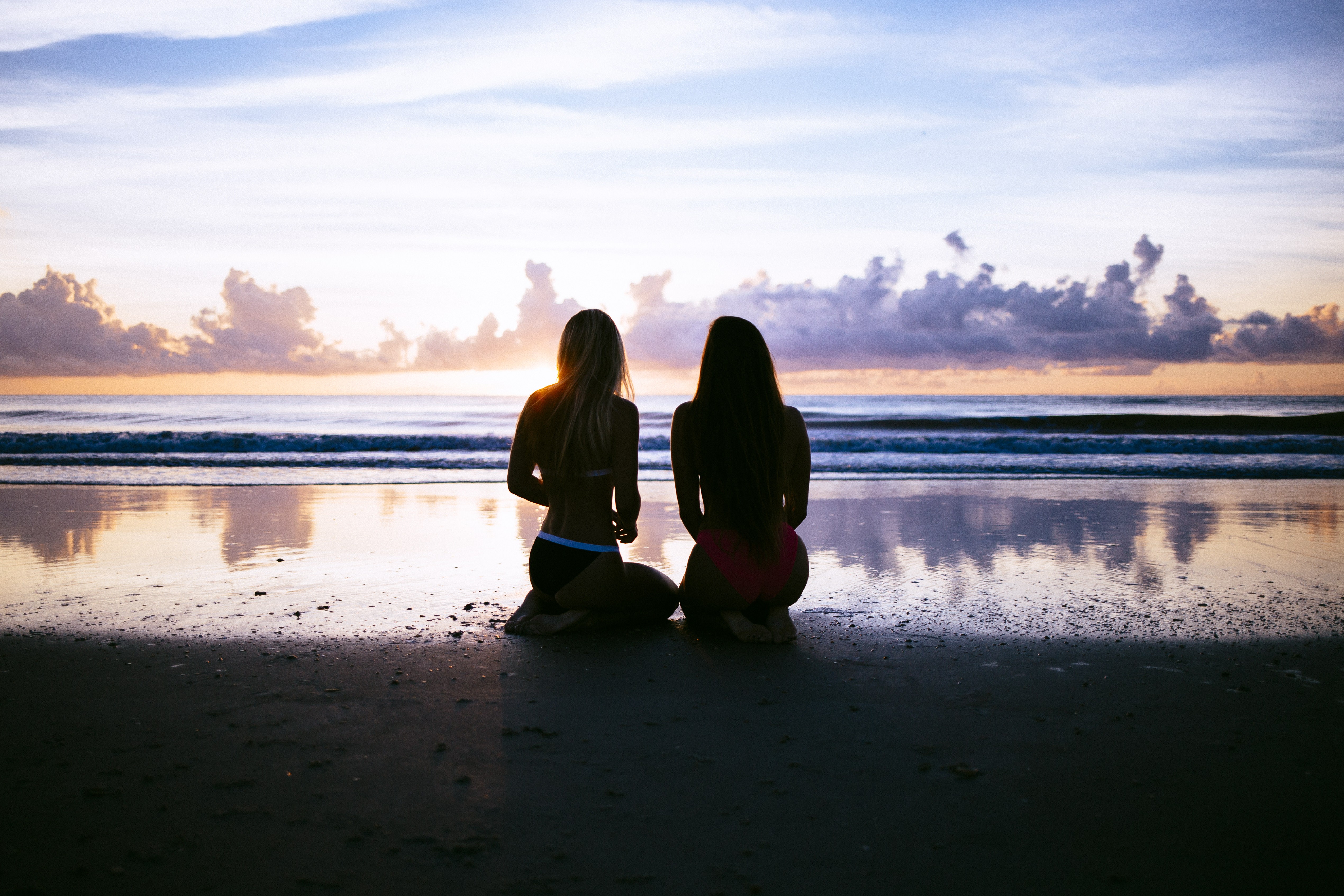 Two women kneeling on a beach at sunset HD Wallpaper