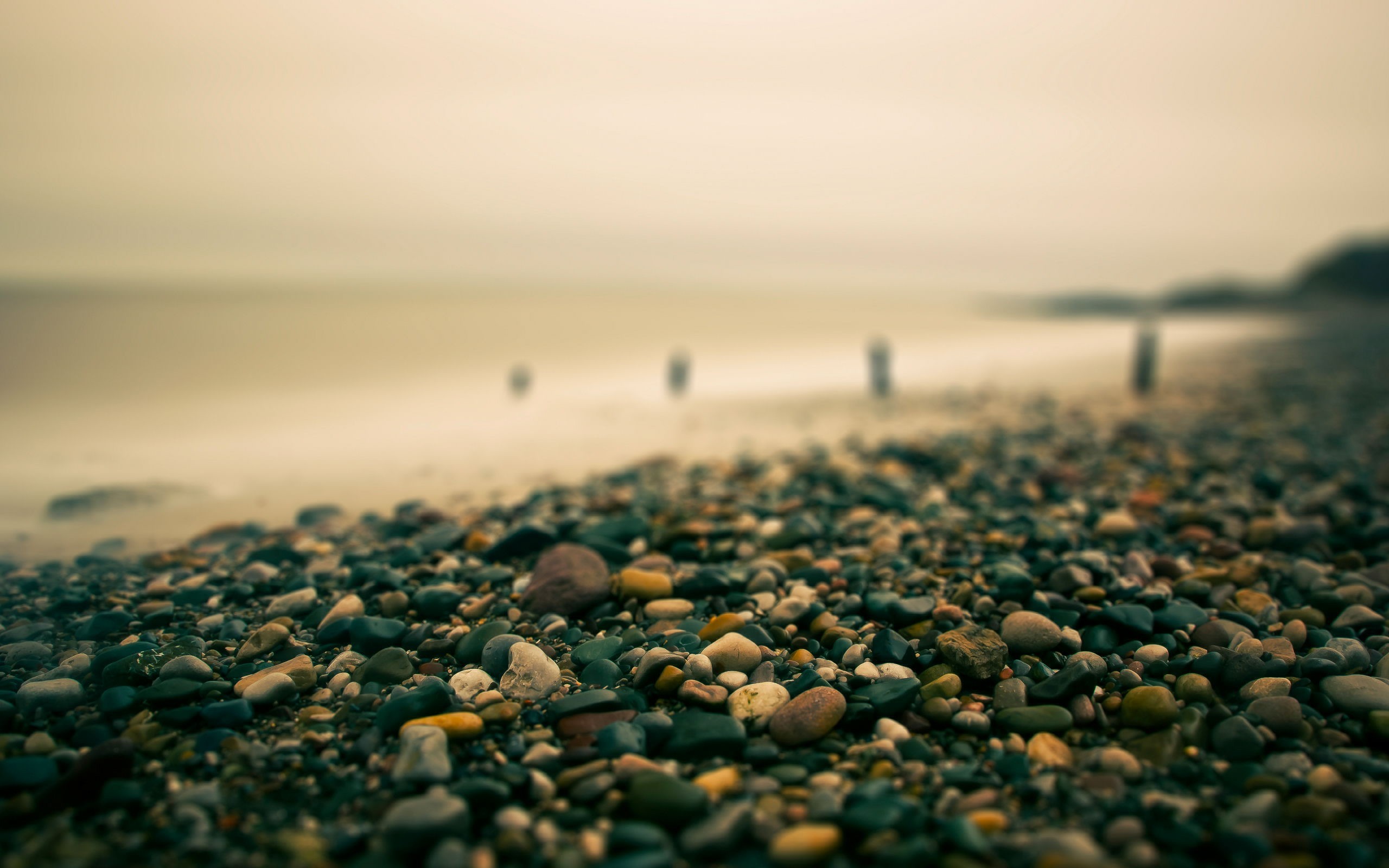 Pebble beach with blurred ocean and posts HD Wallpaper