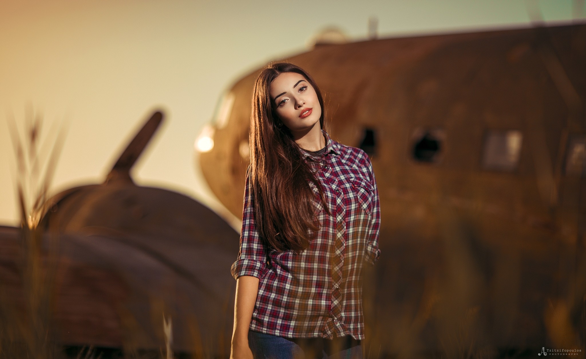Woman in Plaid Shirt Poses Near Airplane Wreckage at Sunset HD Wallpaper