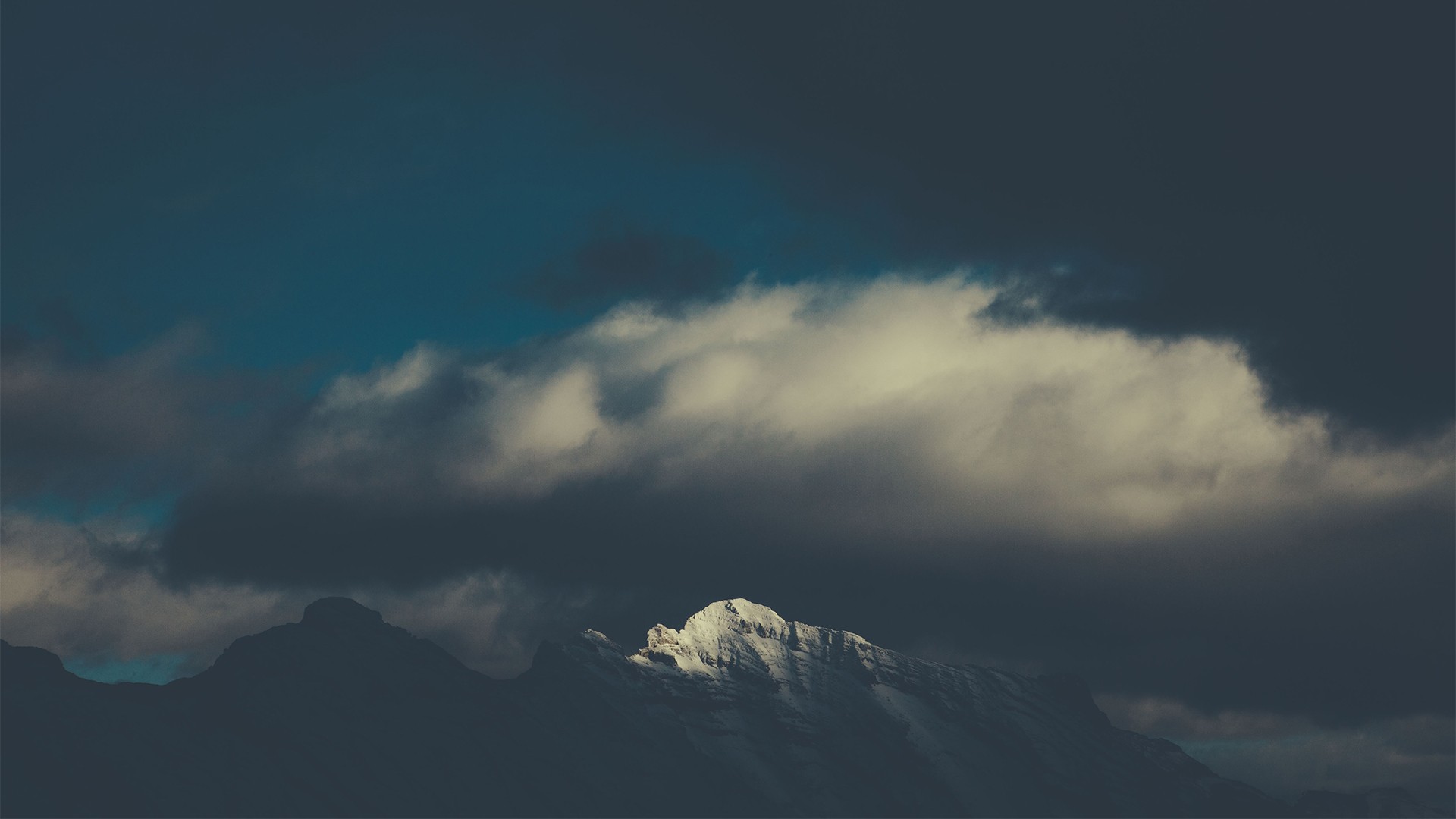 Snowy mountain peak emerges from dark clouds HD Wallpaper