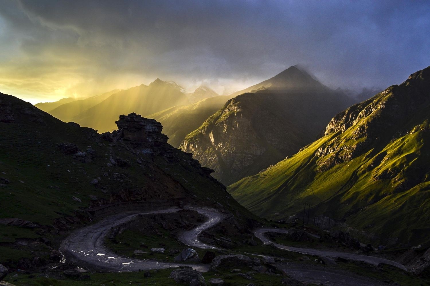 Sunlight streams through mountains onto a winding dirt road in India HD Wallpaper