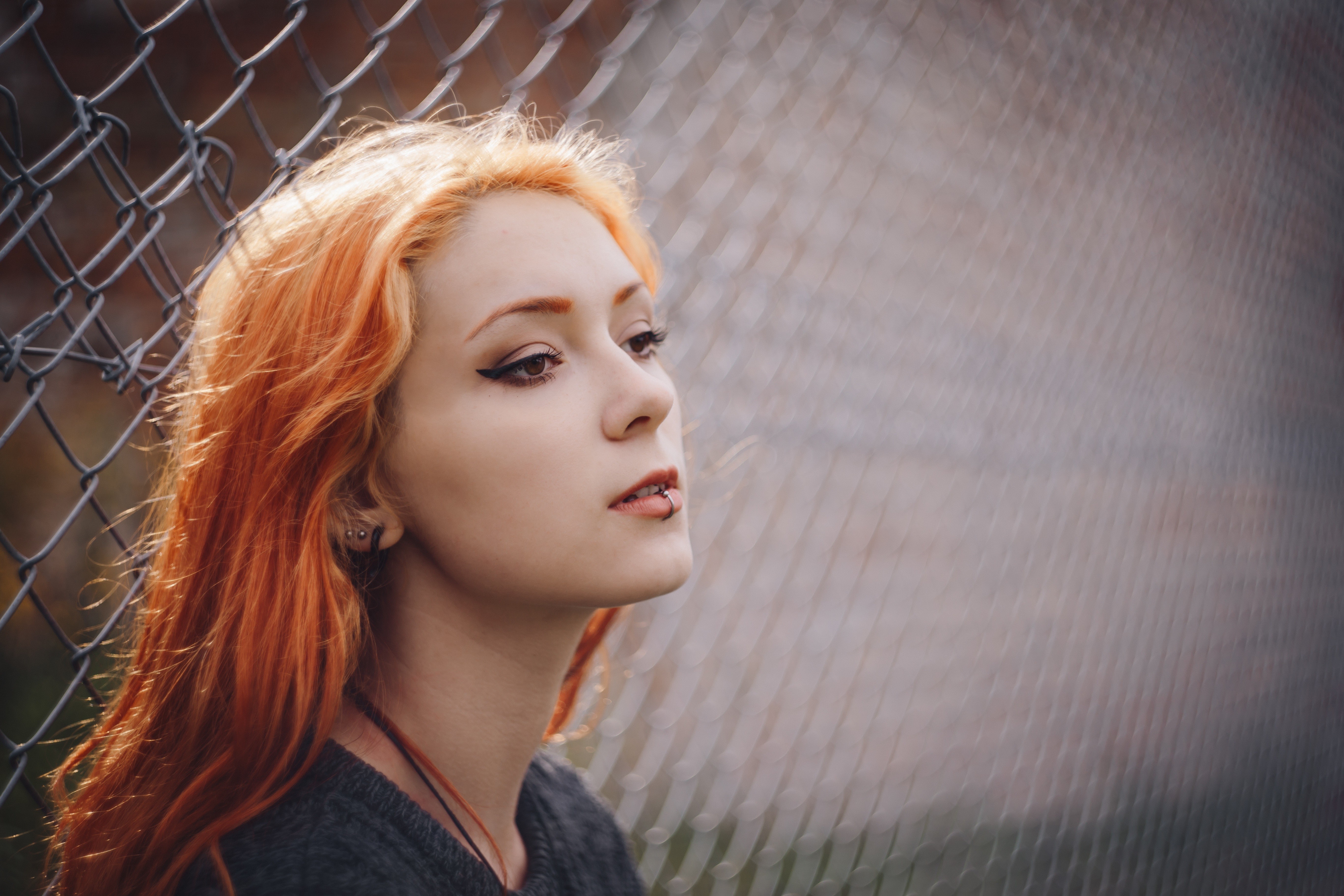 Woman with orange hair and lip piercing by a fence HD Wallpaper