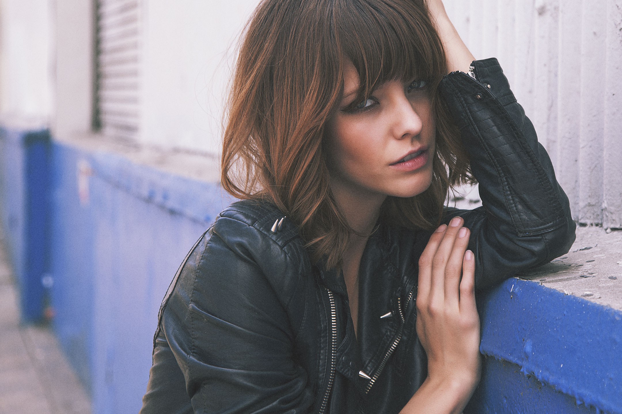 Woman in leather jacket leaning on a blue wall HD Wallpaper