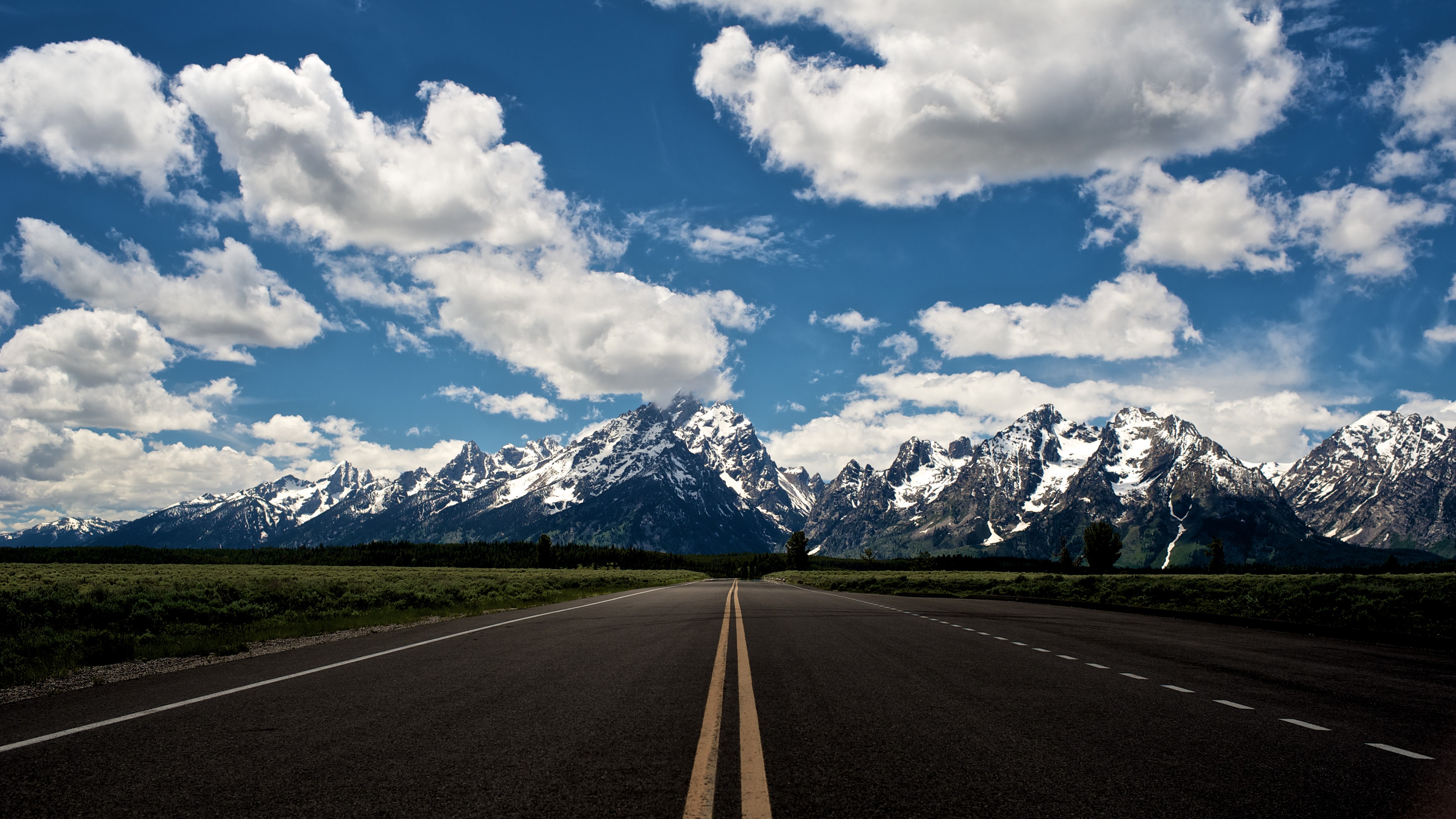 Road leading to snow-capped mountains under a cloudy sky HD Wallpaper