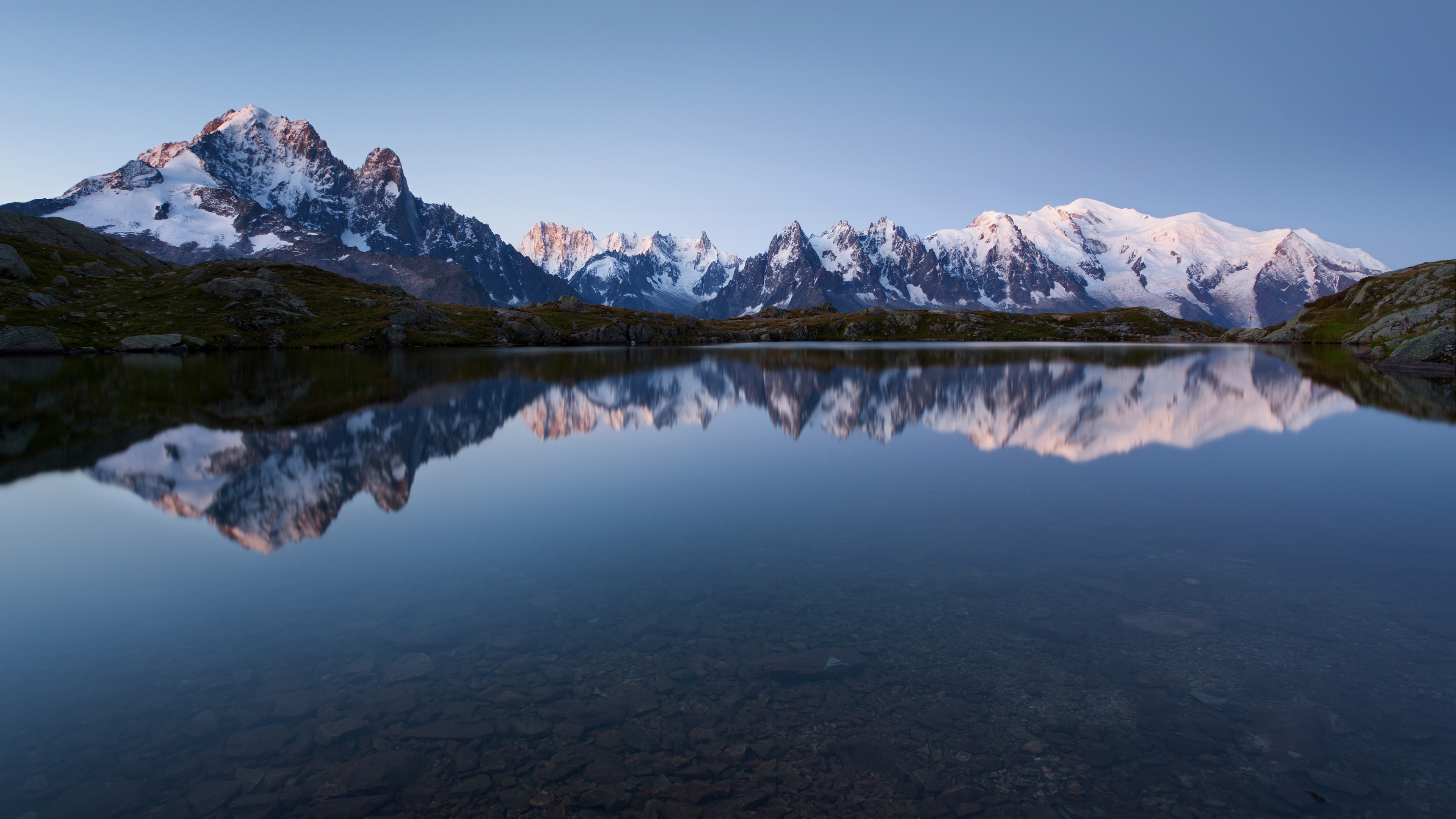 Snow-capped mountains reflected in a calm lake at sunrise HD Wallpaper