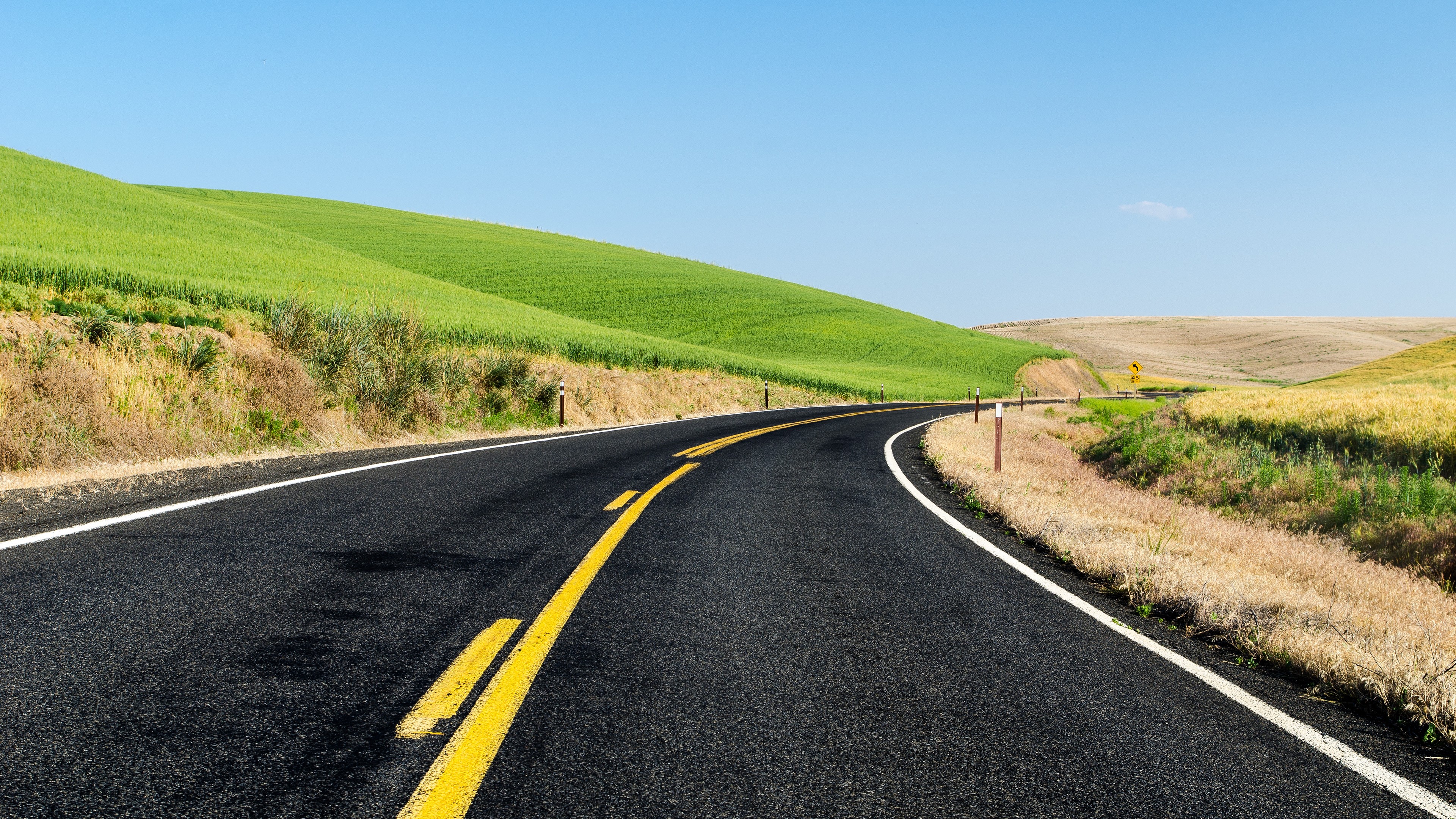 Curving asphalt road through rolling green hills HD Wallpaper