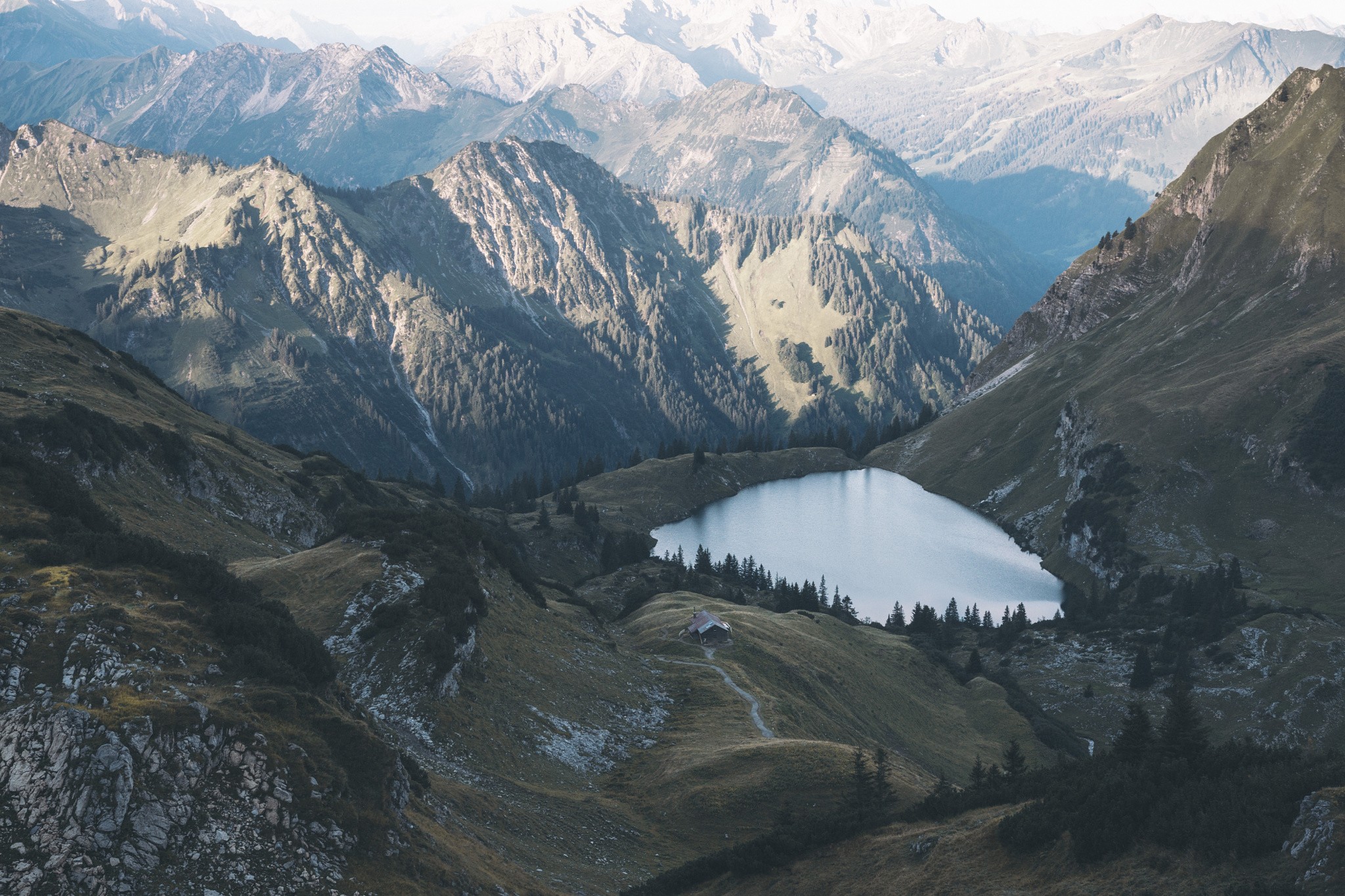 Lake nestled in a mountain valley with a small cabin HD Wallpaper
