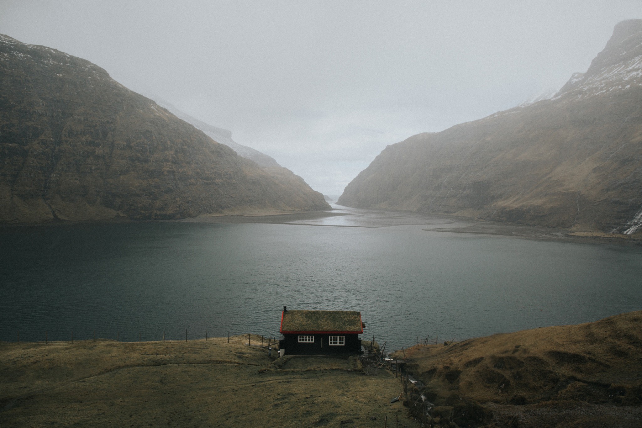 A remote cabin by a lake in a misty mountain landscape HD Wallpaper