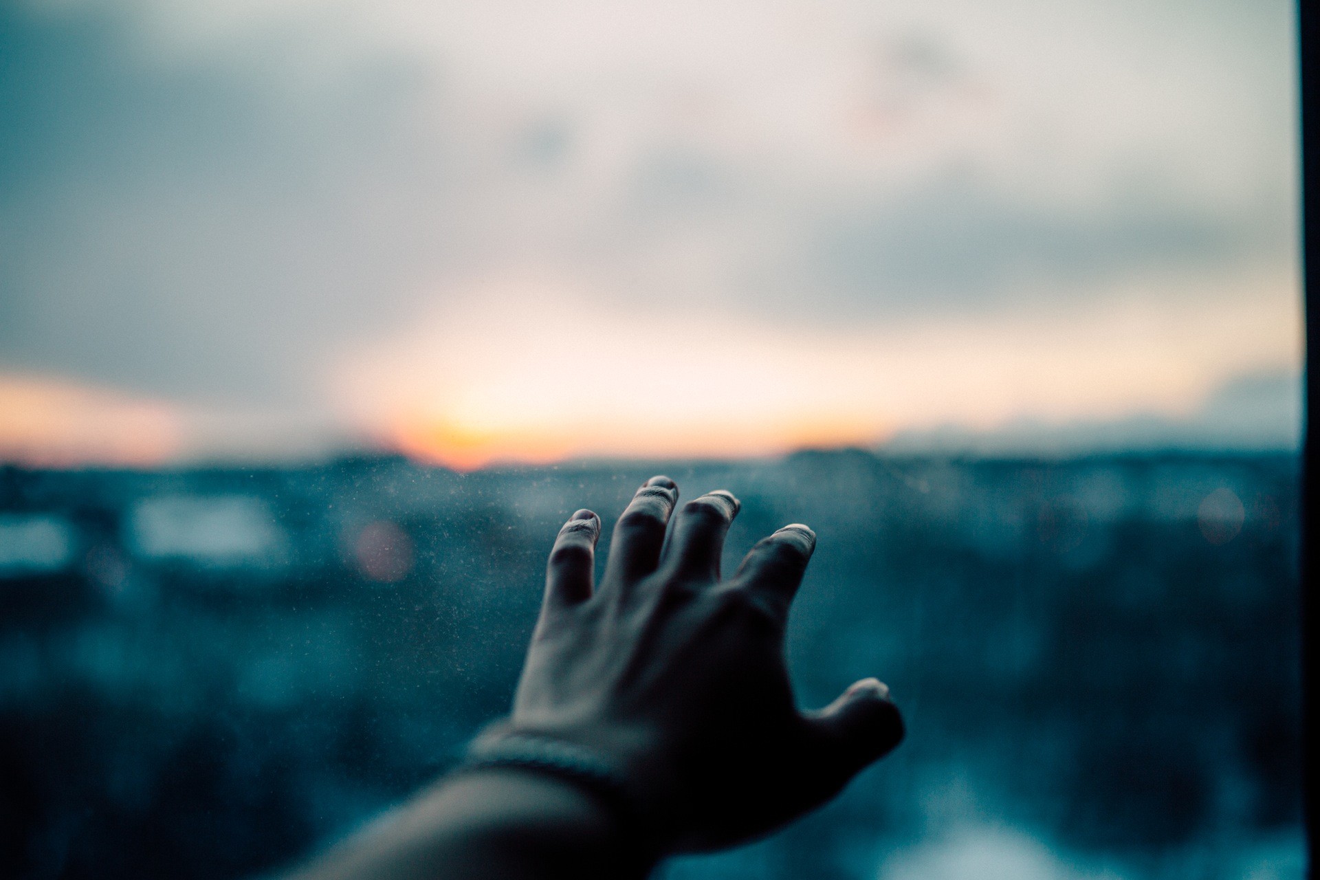 Hand reaching out towards a sunset over a city HD Wallpaper