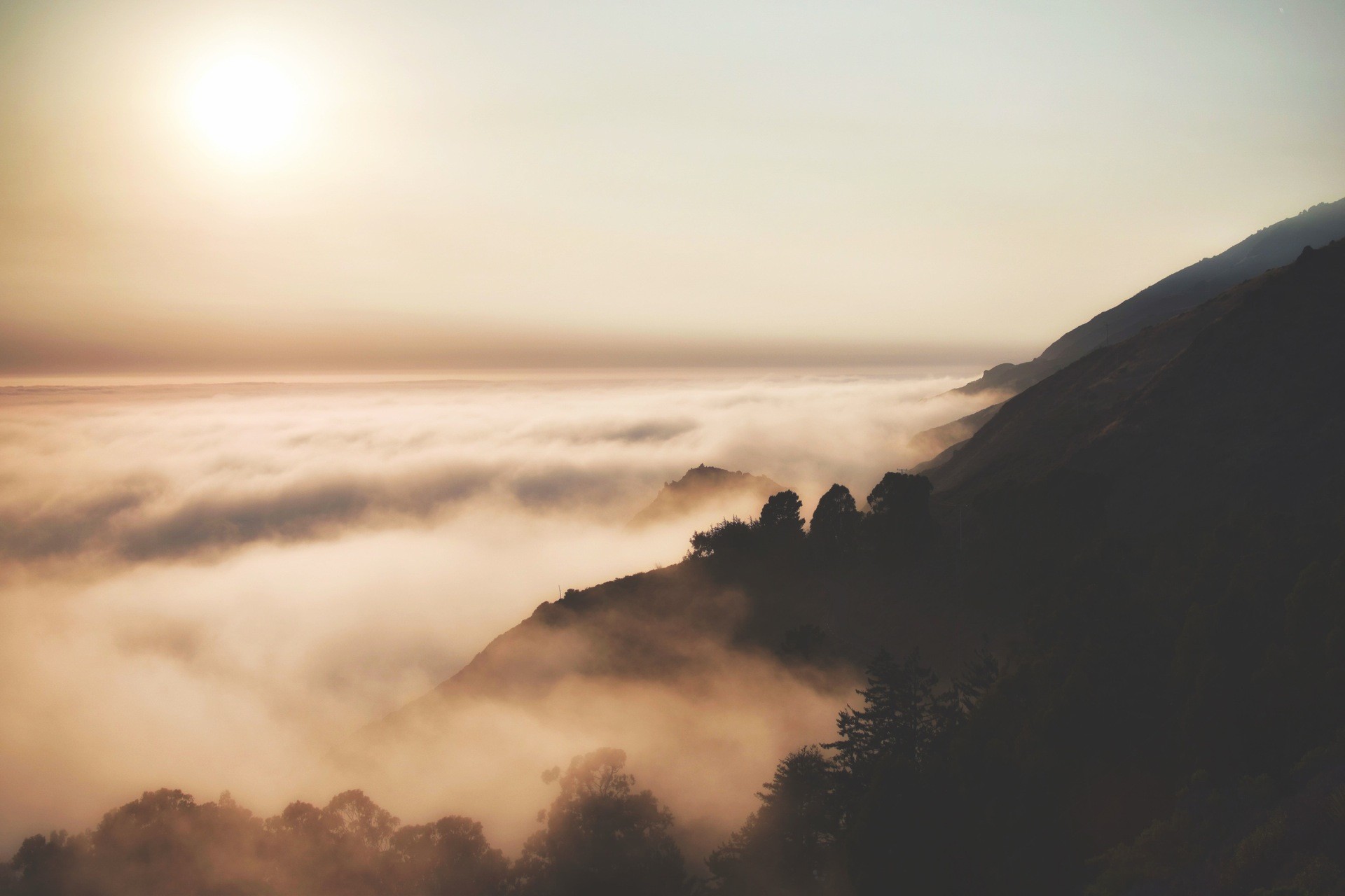 Mountain pass covered in mist with sunlit sky HD Wallpaper