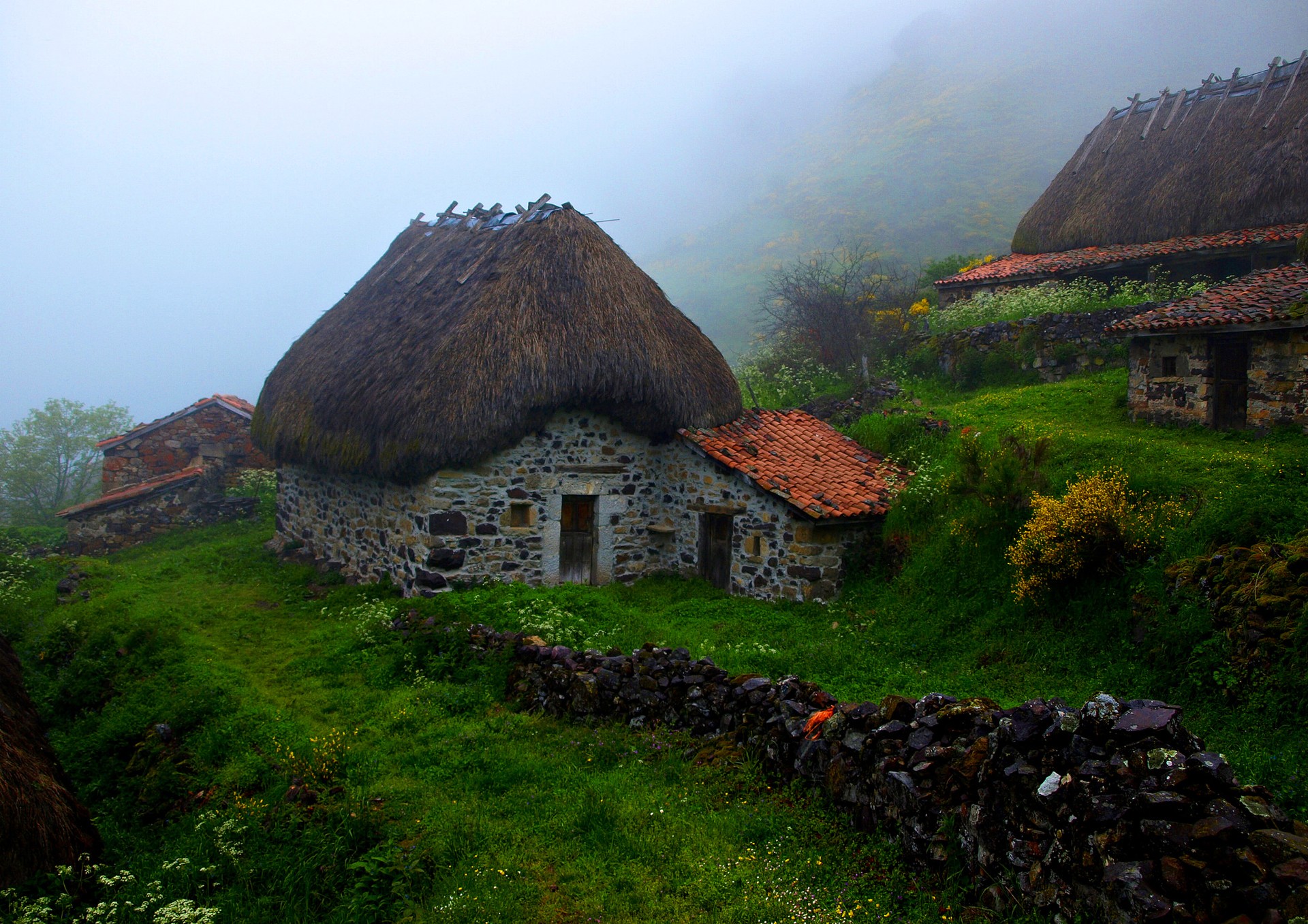 Stone houses with thatched roofs in the mist HD Wallpaper