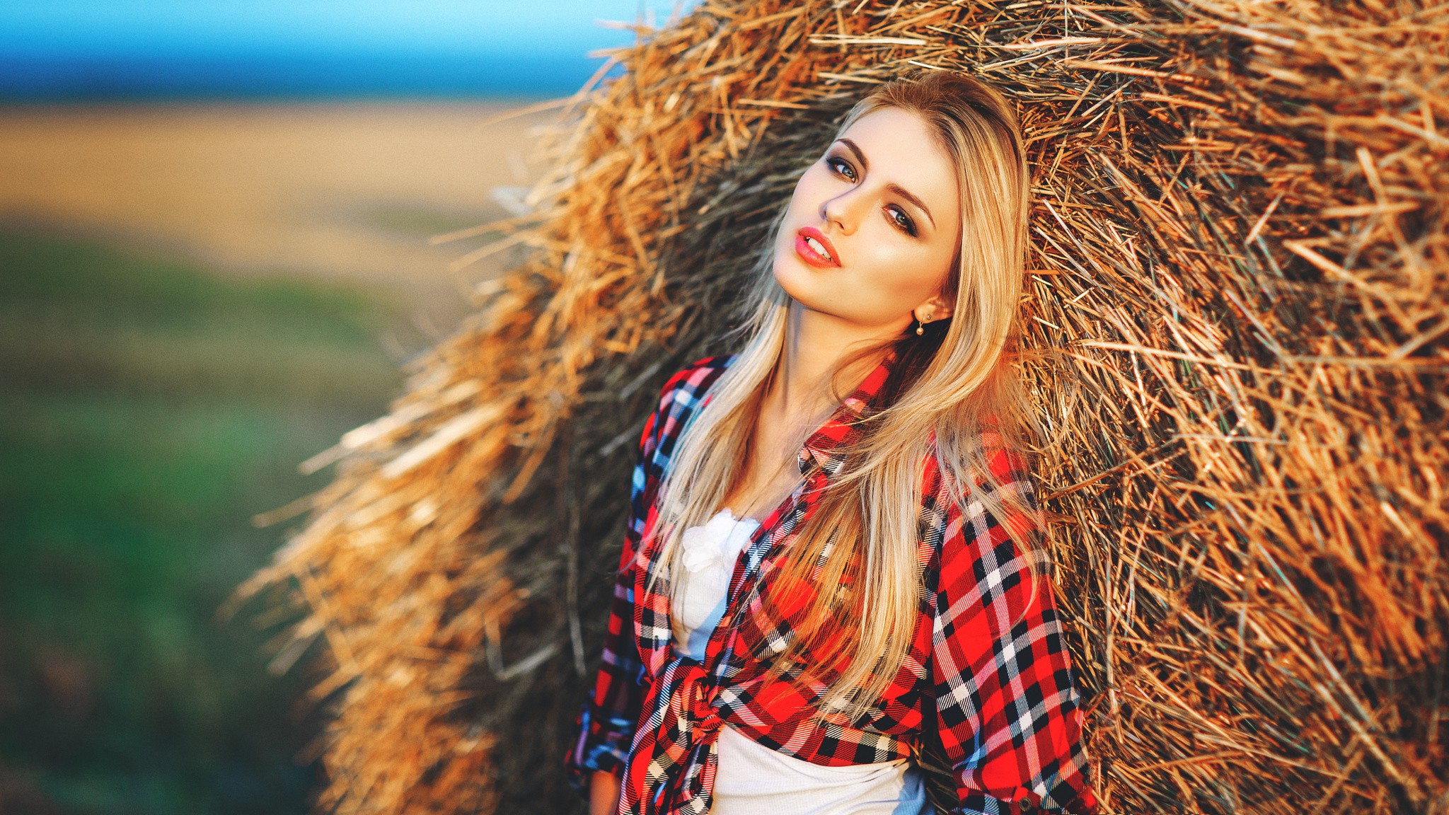 Blonde woman in plaid shirt leaning on hay bale HD Wallpaper
