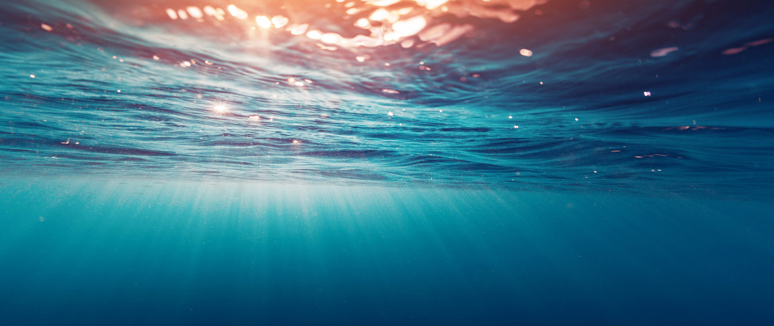 Underwater view of sunlight filtering through ocean waves HD Wallpaper