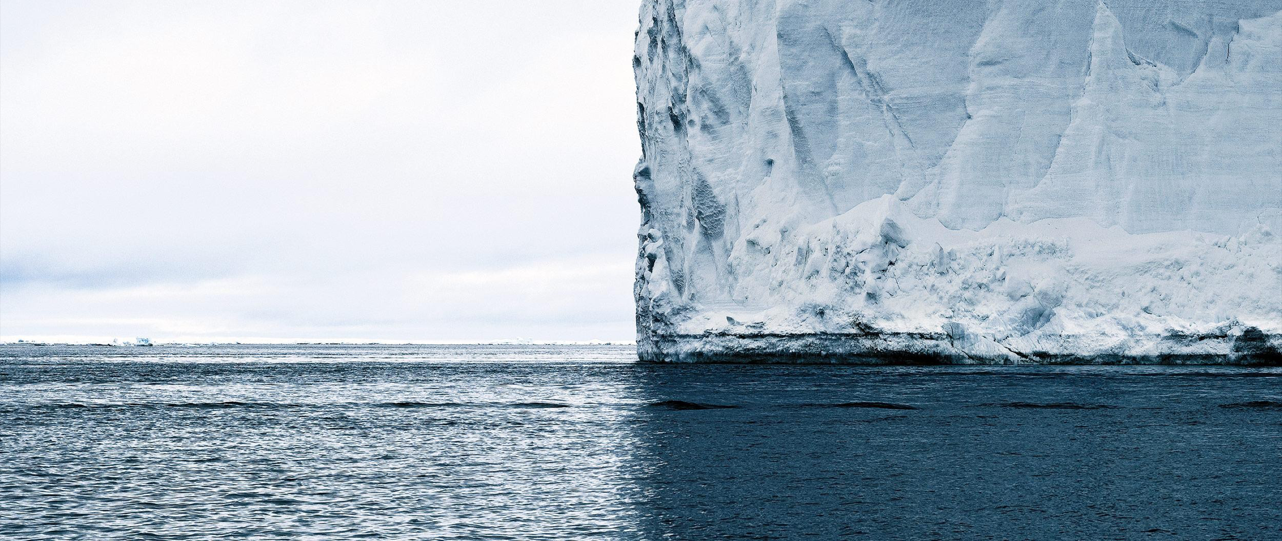 Massive iceberg in the ocean under a cloudy sky HD Wallpaper