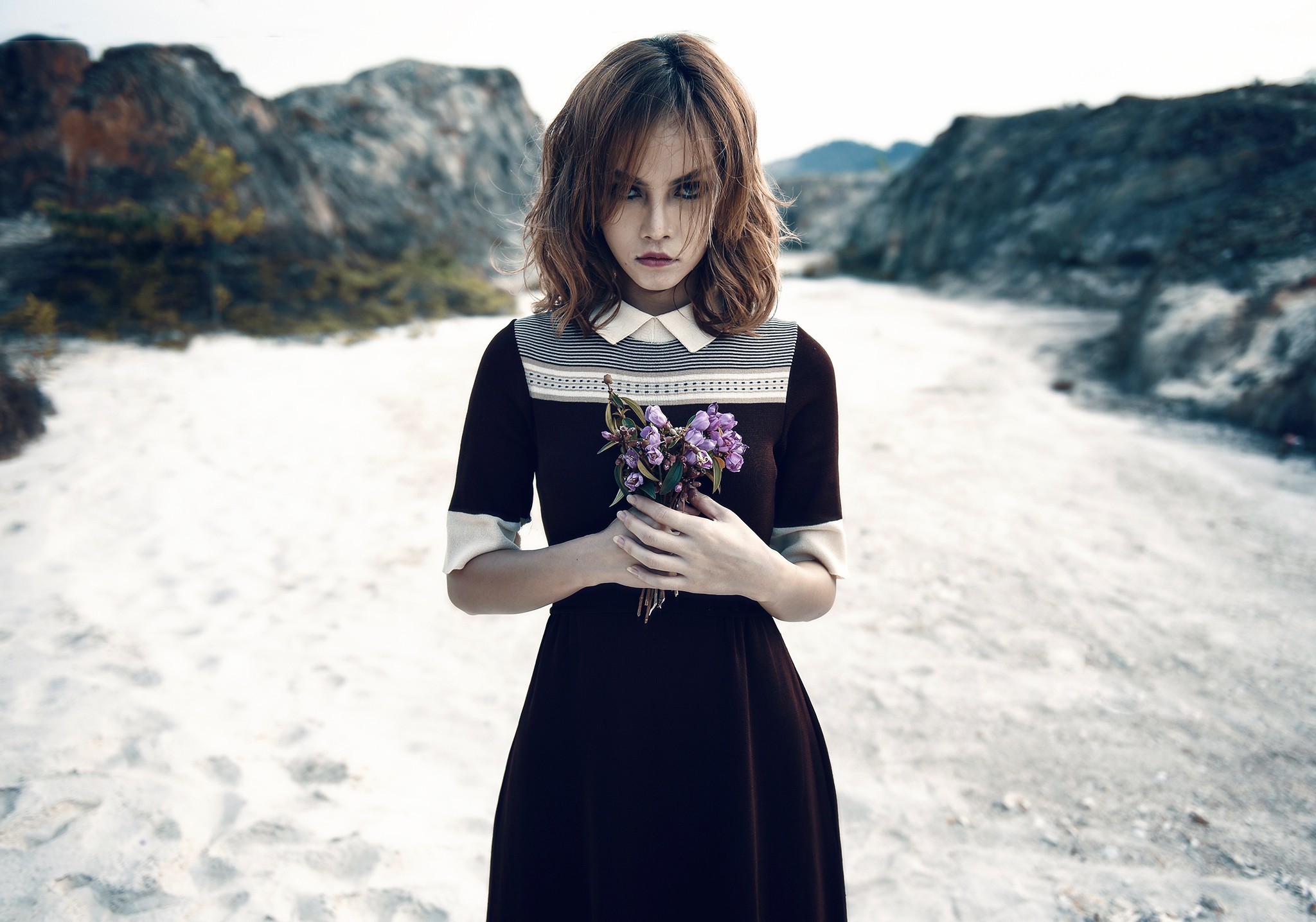 Woman in dress holding flowers in a barren landscape HD Wallpaper
