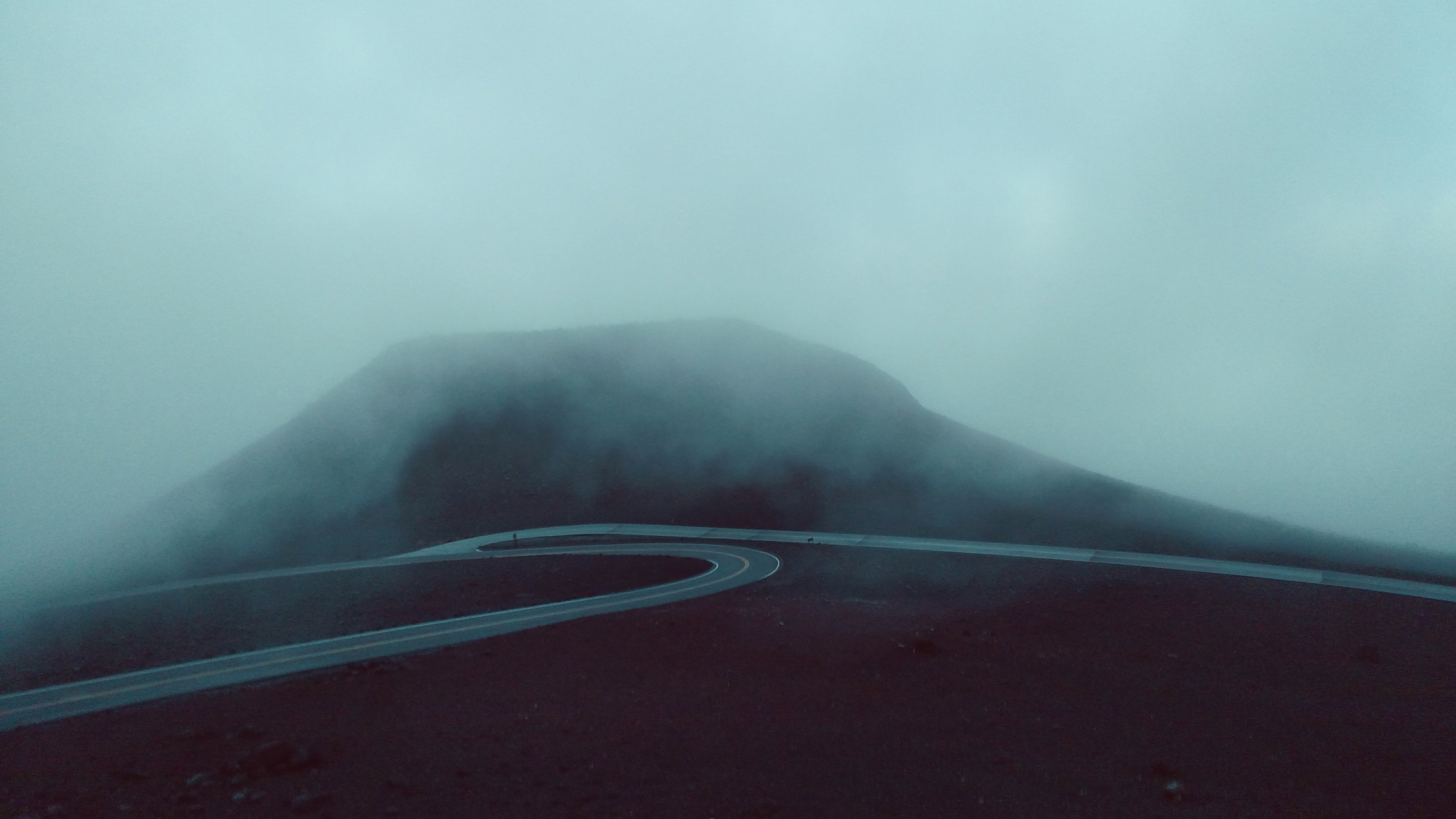 Misty mountain road winding through fog HD Wallpaper