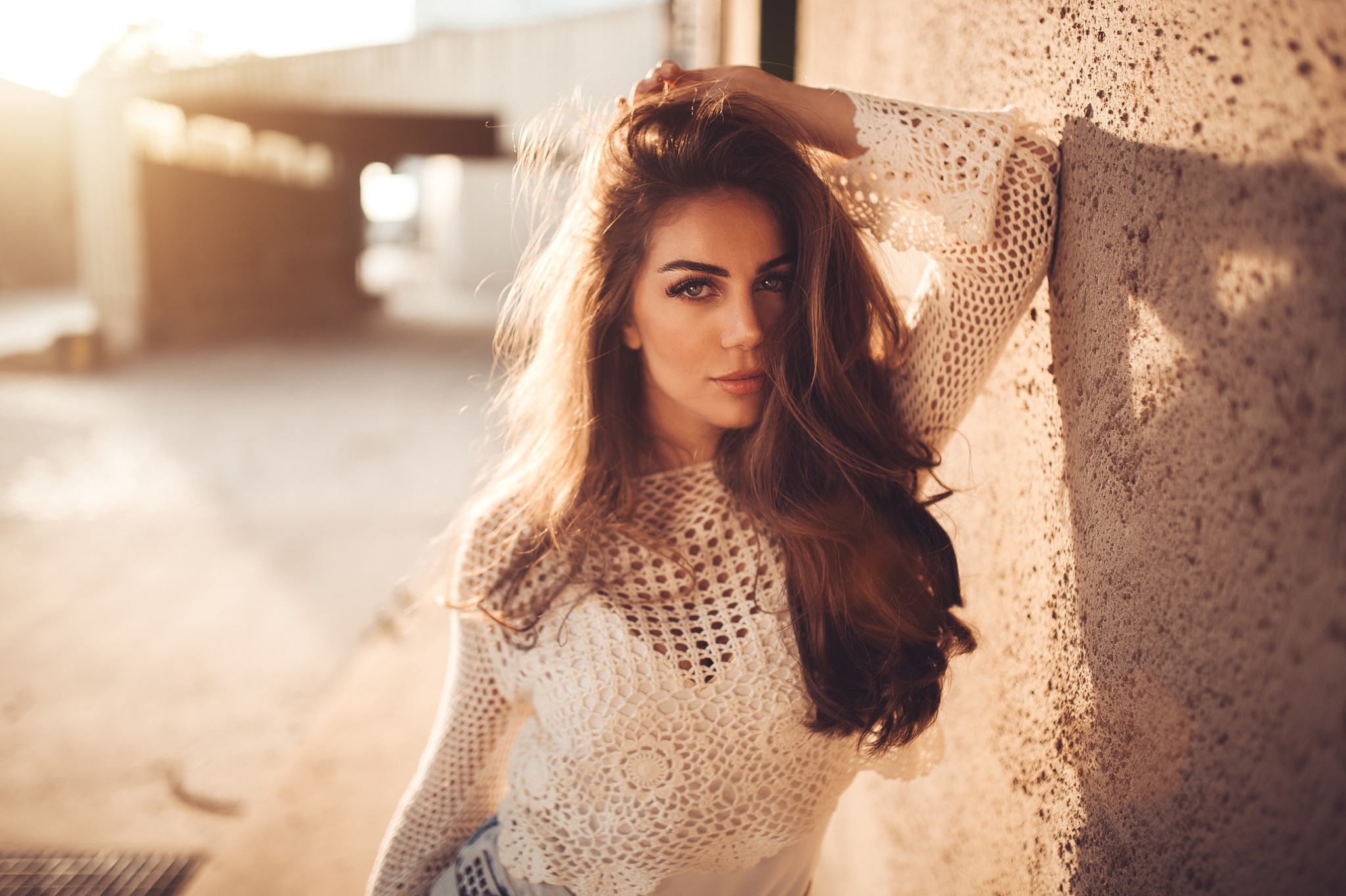 Woman with hands on head leaning against a wall at sunset HD Wallpaper