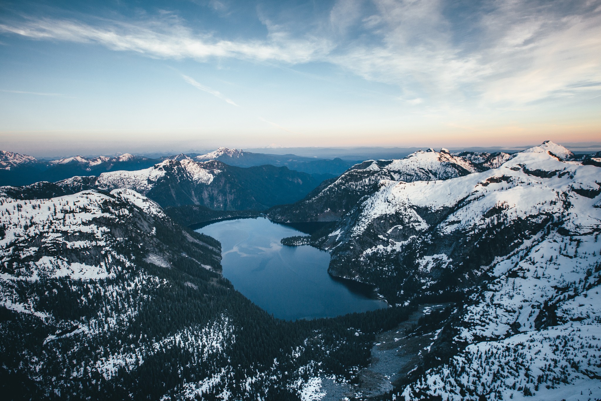 Snow-capped mountains surround a dark lake HD Wallpaper