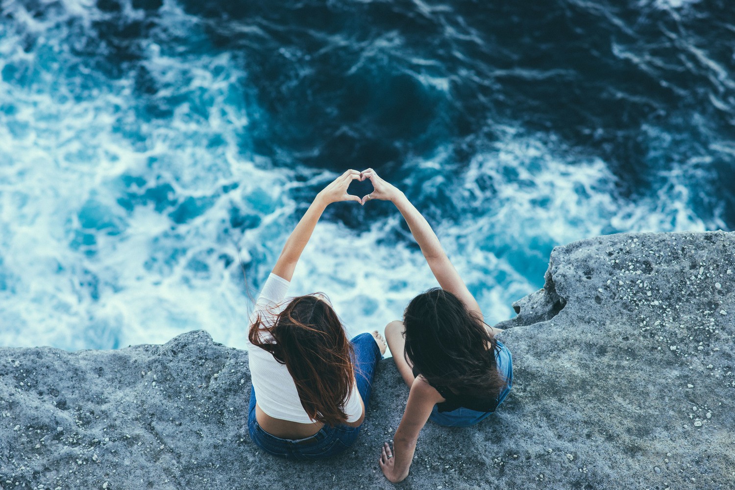 Two women form a heart shape over the sea HD Wallpaper