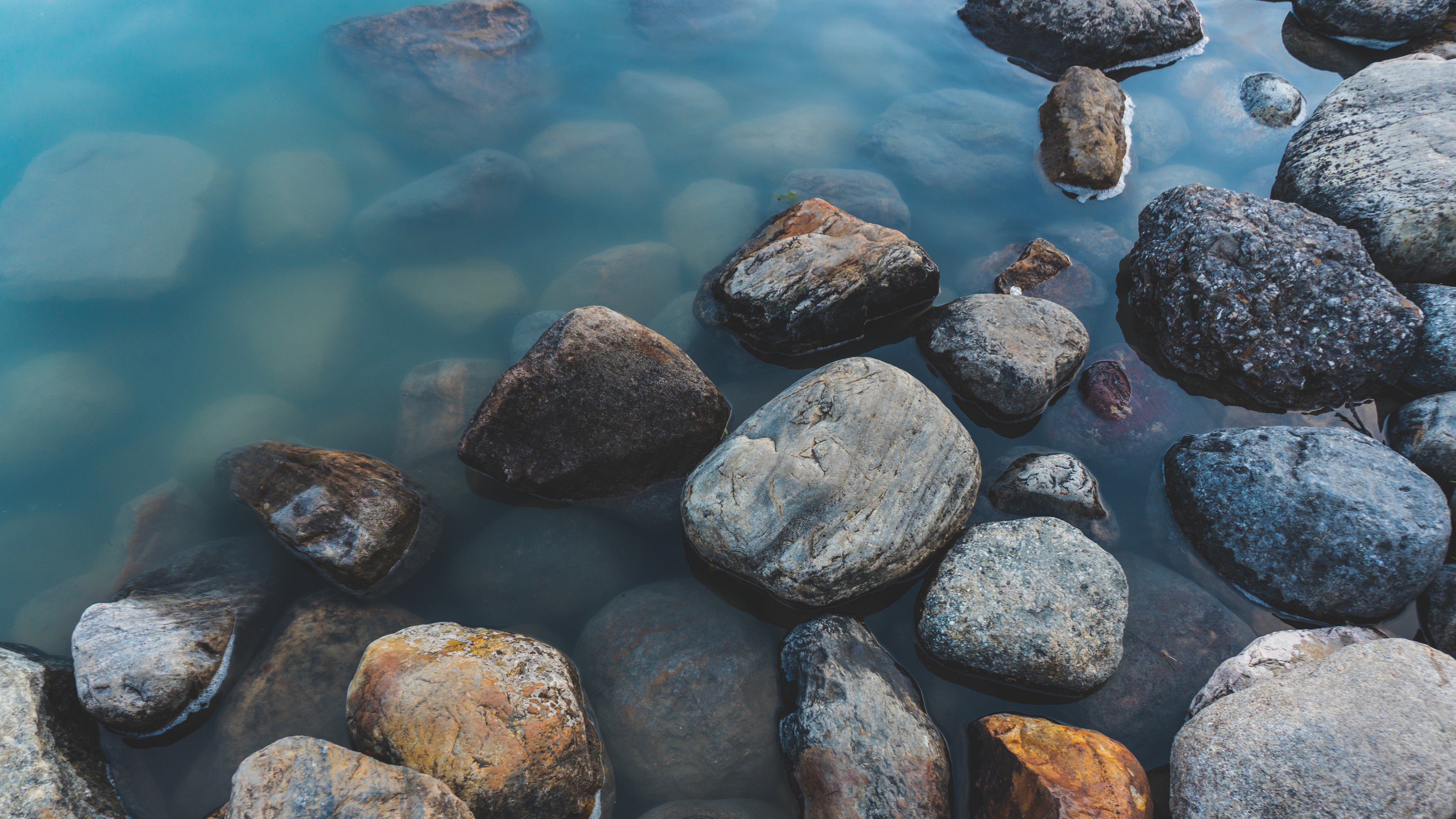 Smooth rocks submerged in clear blue water HD Wallpaper
