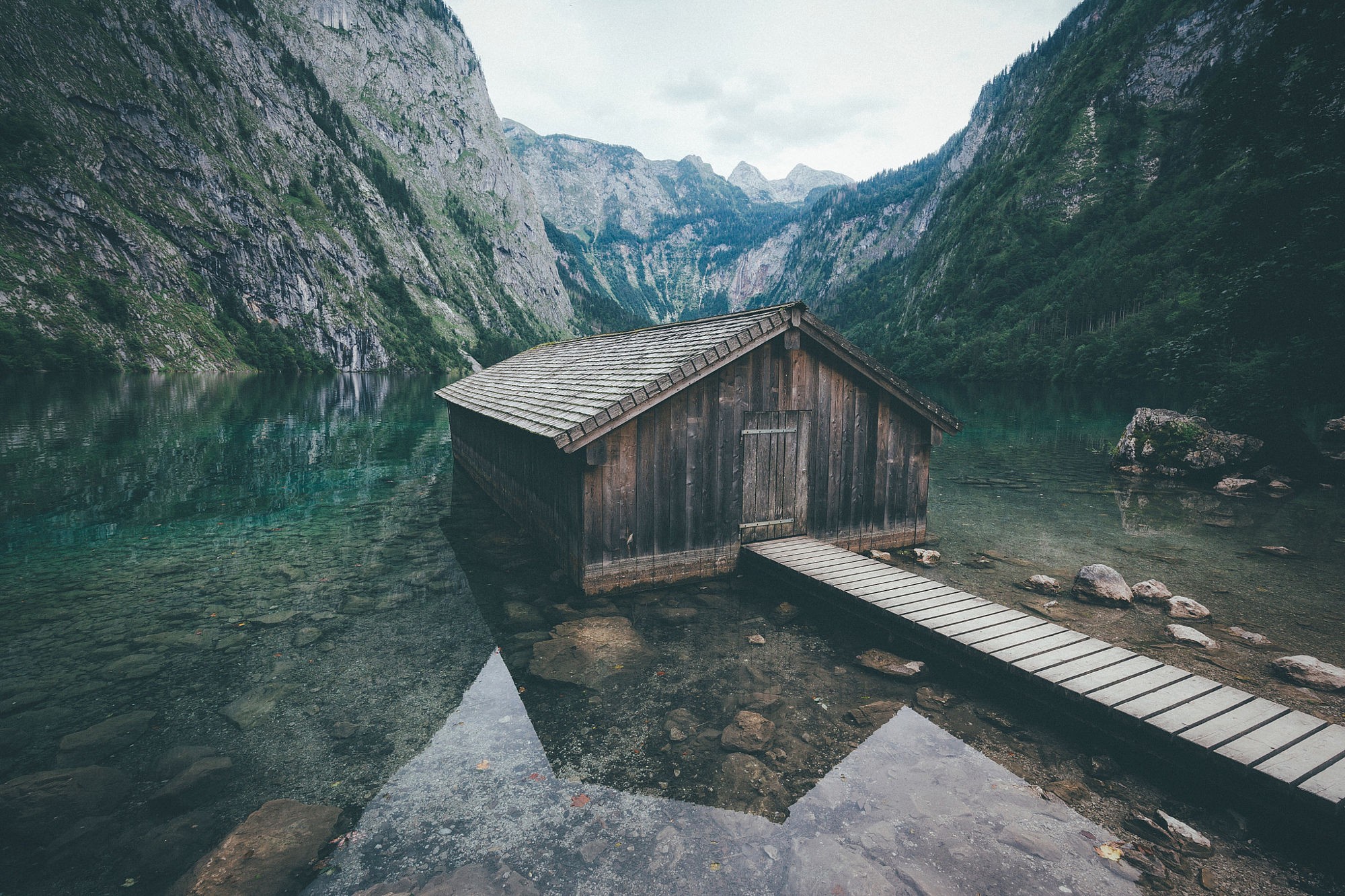 Wooden hut on a clear lake surrounded by mountains HD Wallpaper