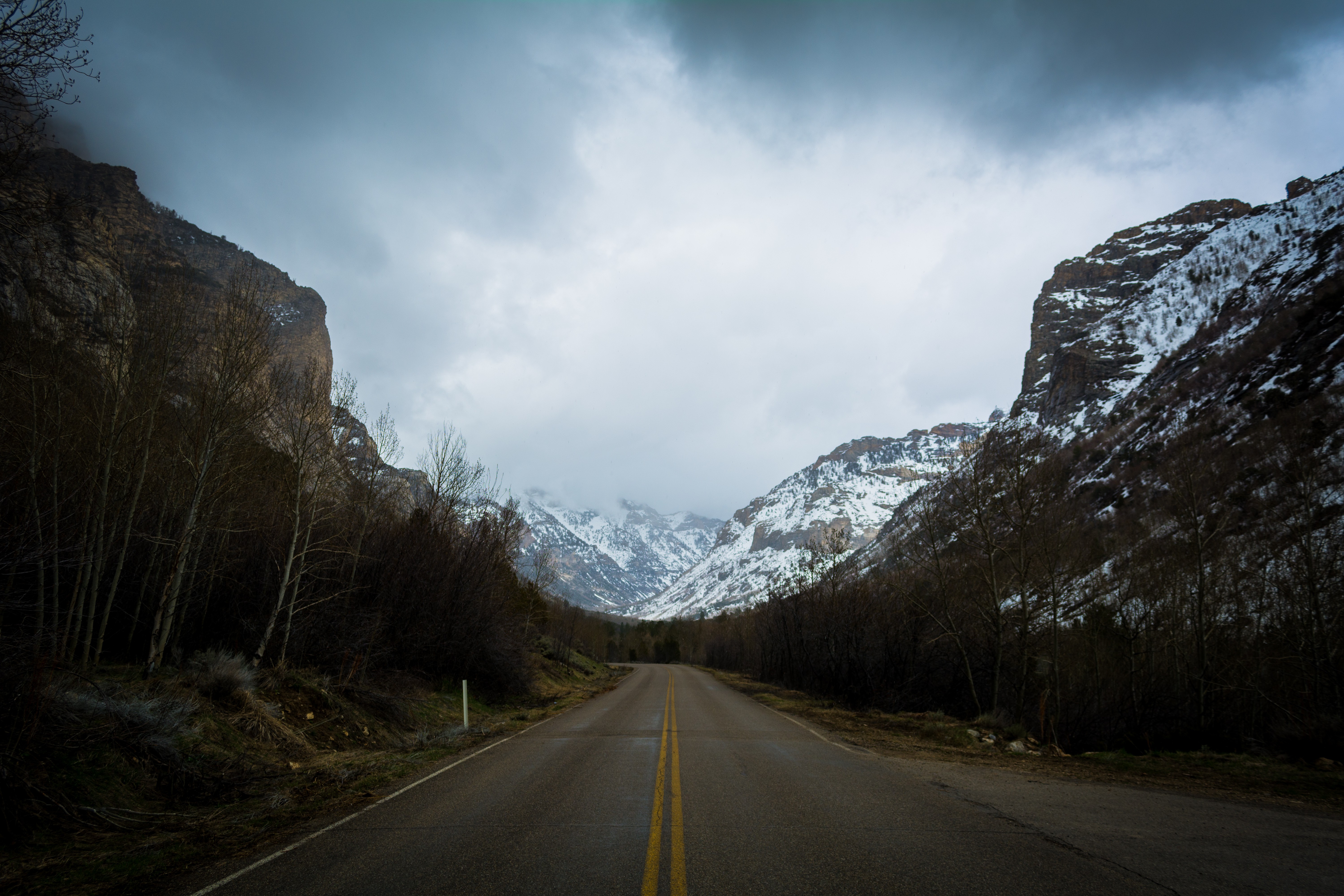 Road through snowy mountains under cloudy sky HD Wallpaper