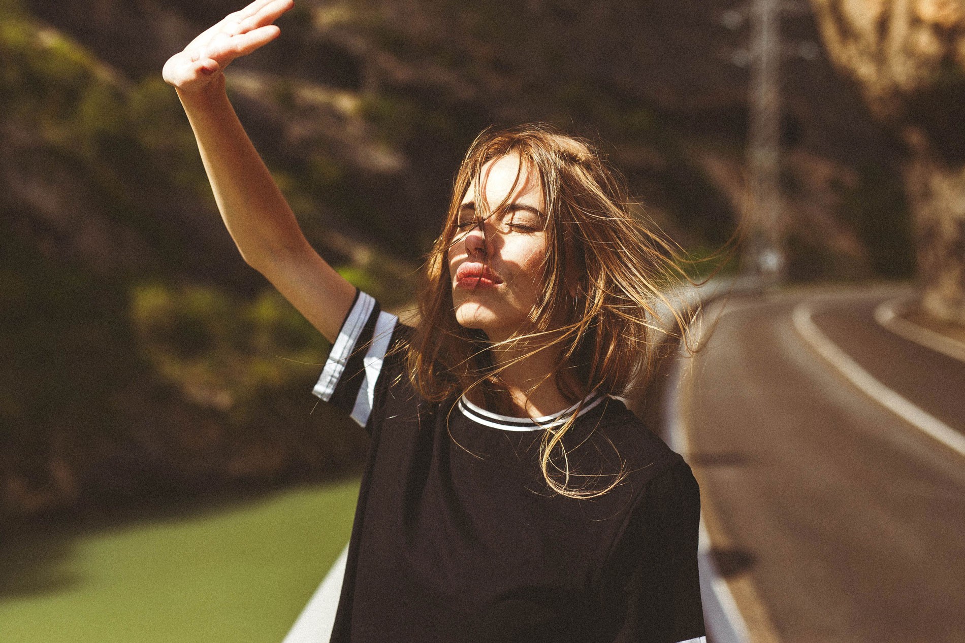 Woman with hair in face shielding eyes from sun on road HD Wallpaper