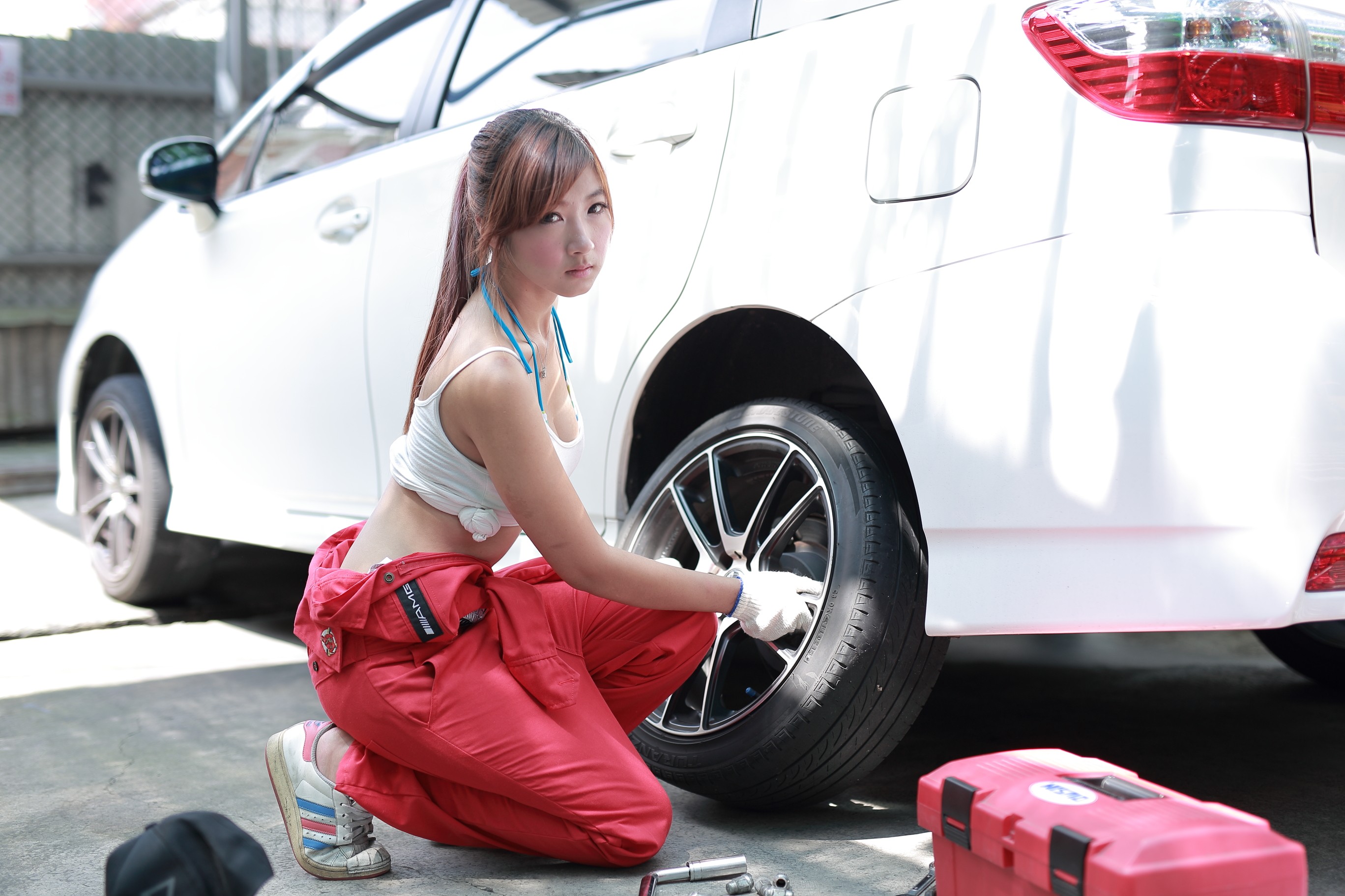 Asian woman in red overalls fixing a car tire HD Wallpaper