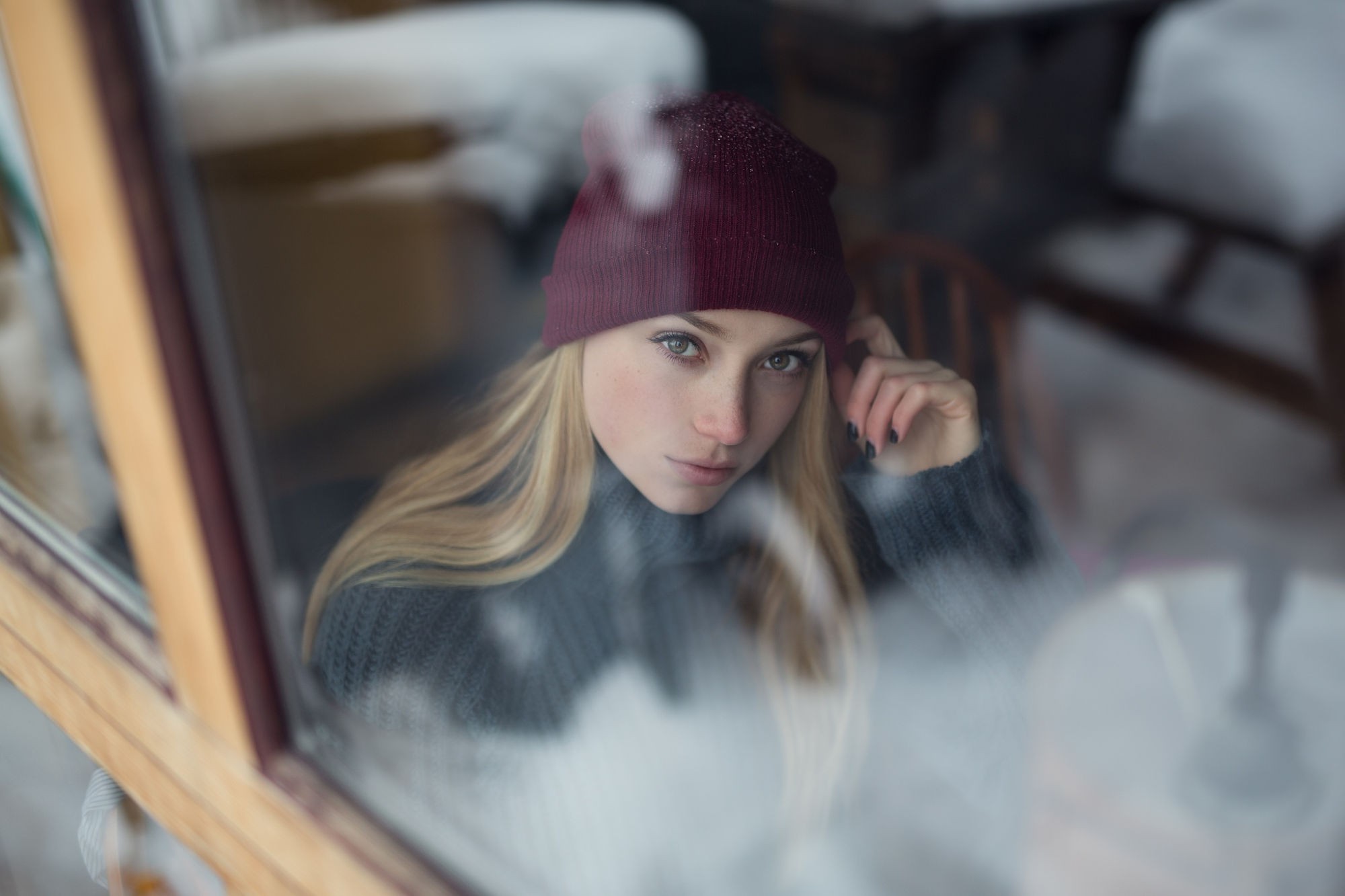 Woman in beanie and sweater looking through window HD Wallpaper