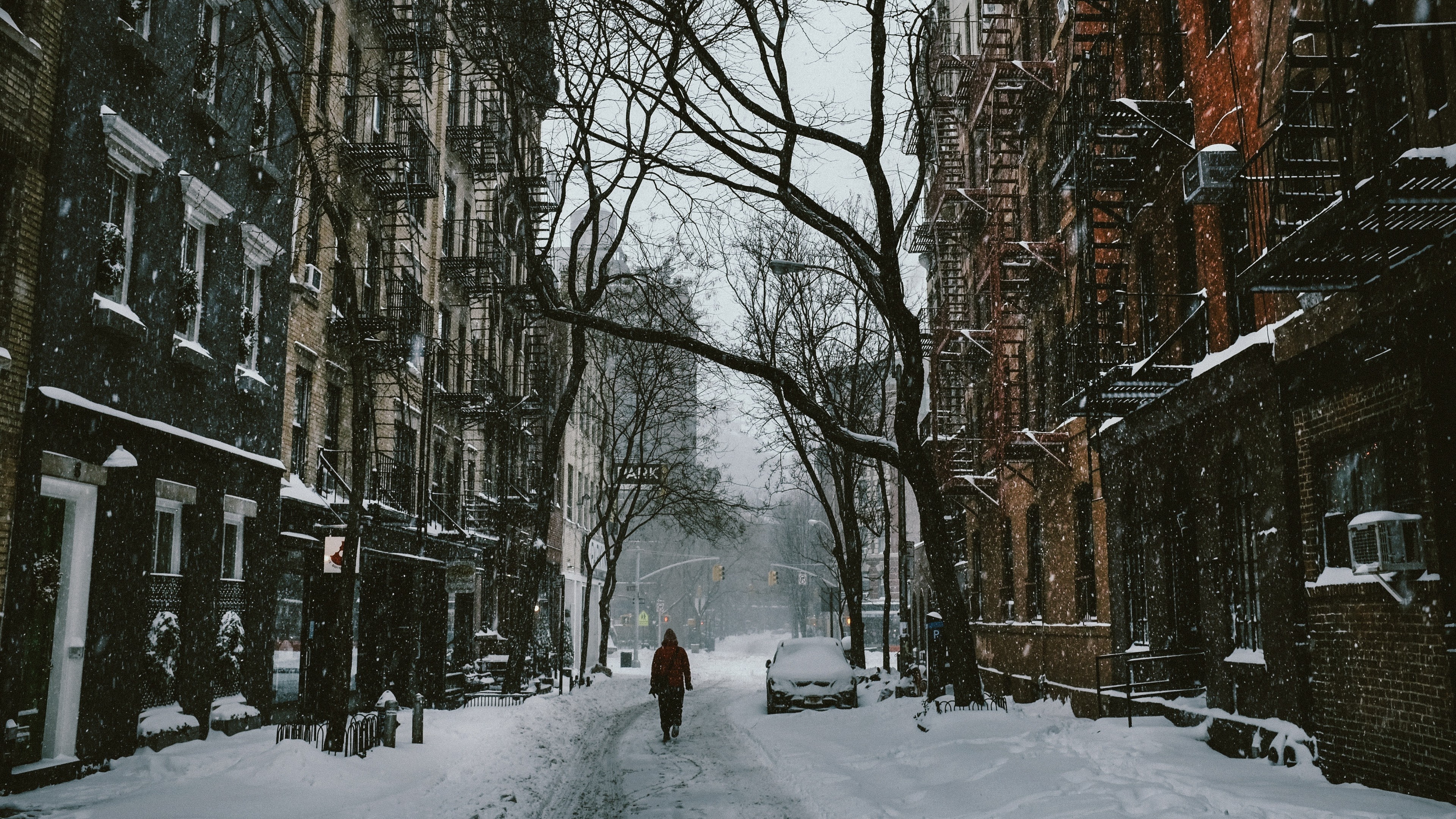 Person walking down a snowy street in a city HD Wallpaper