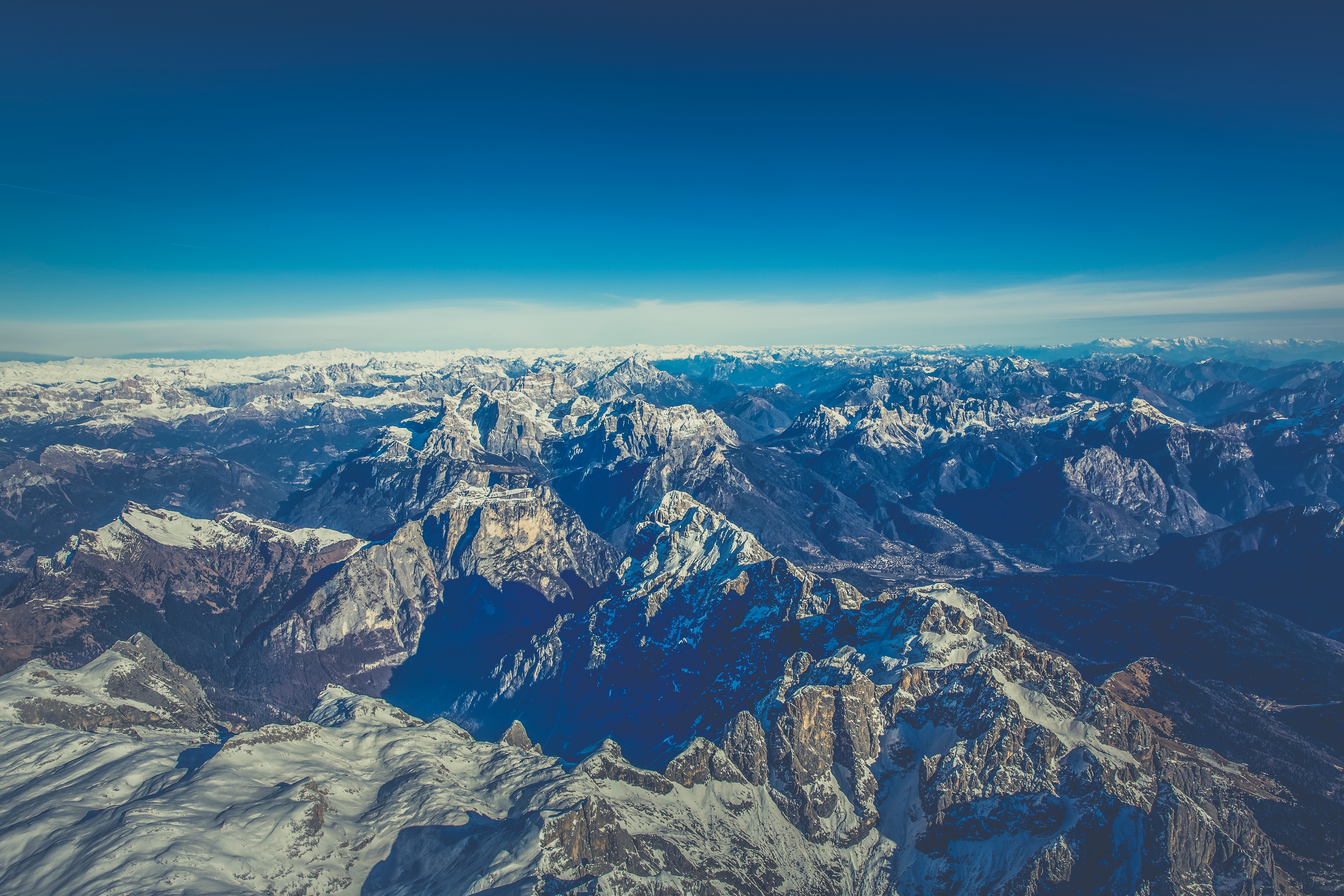 Aerial view of snow-covered mountains under a clear blue sky HD Wallpaper