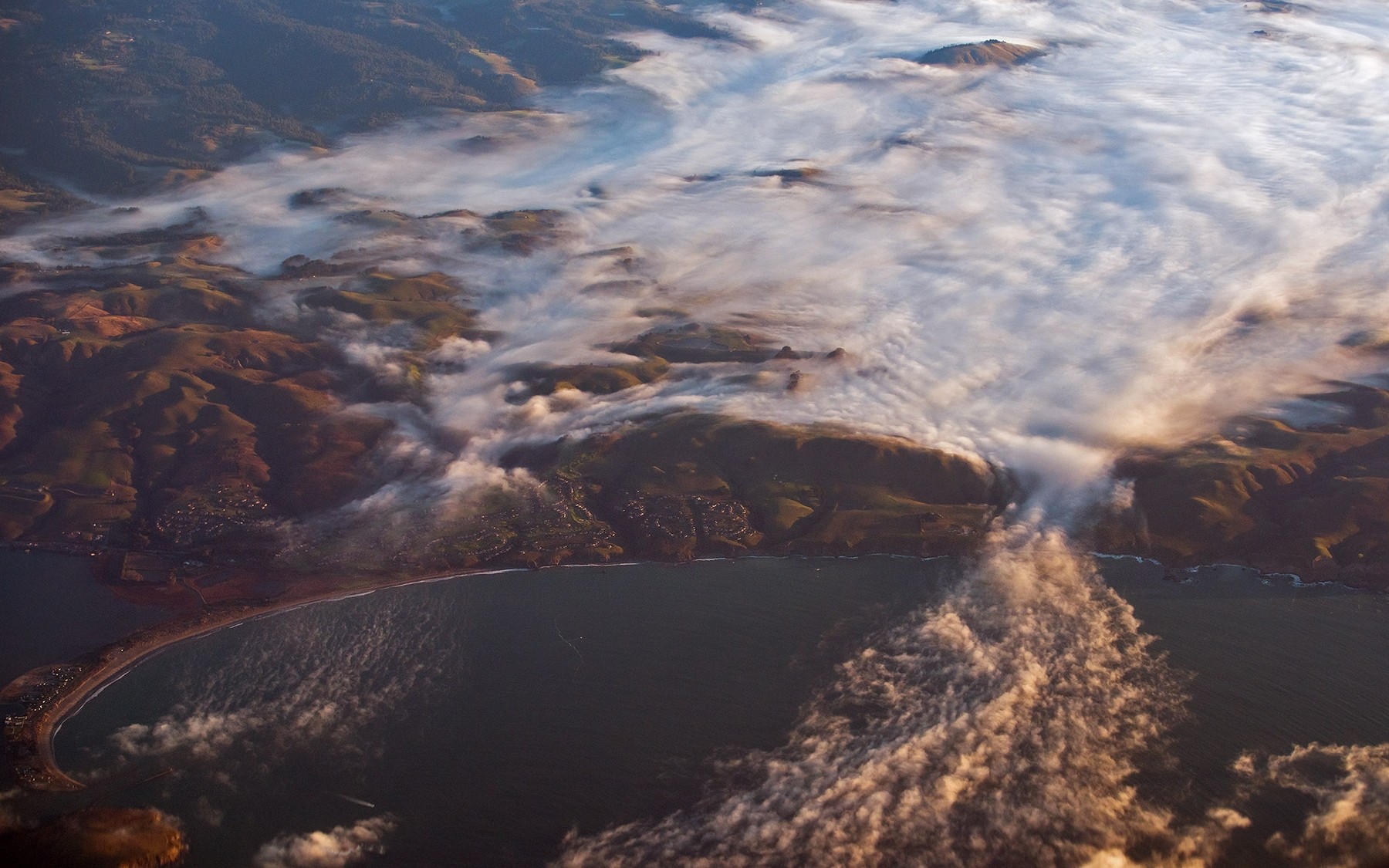 Aerial view of a misty coastline with rolling hills HD Wallpaper