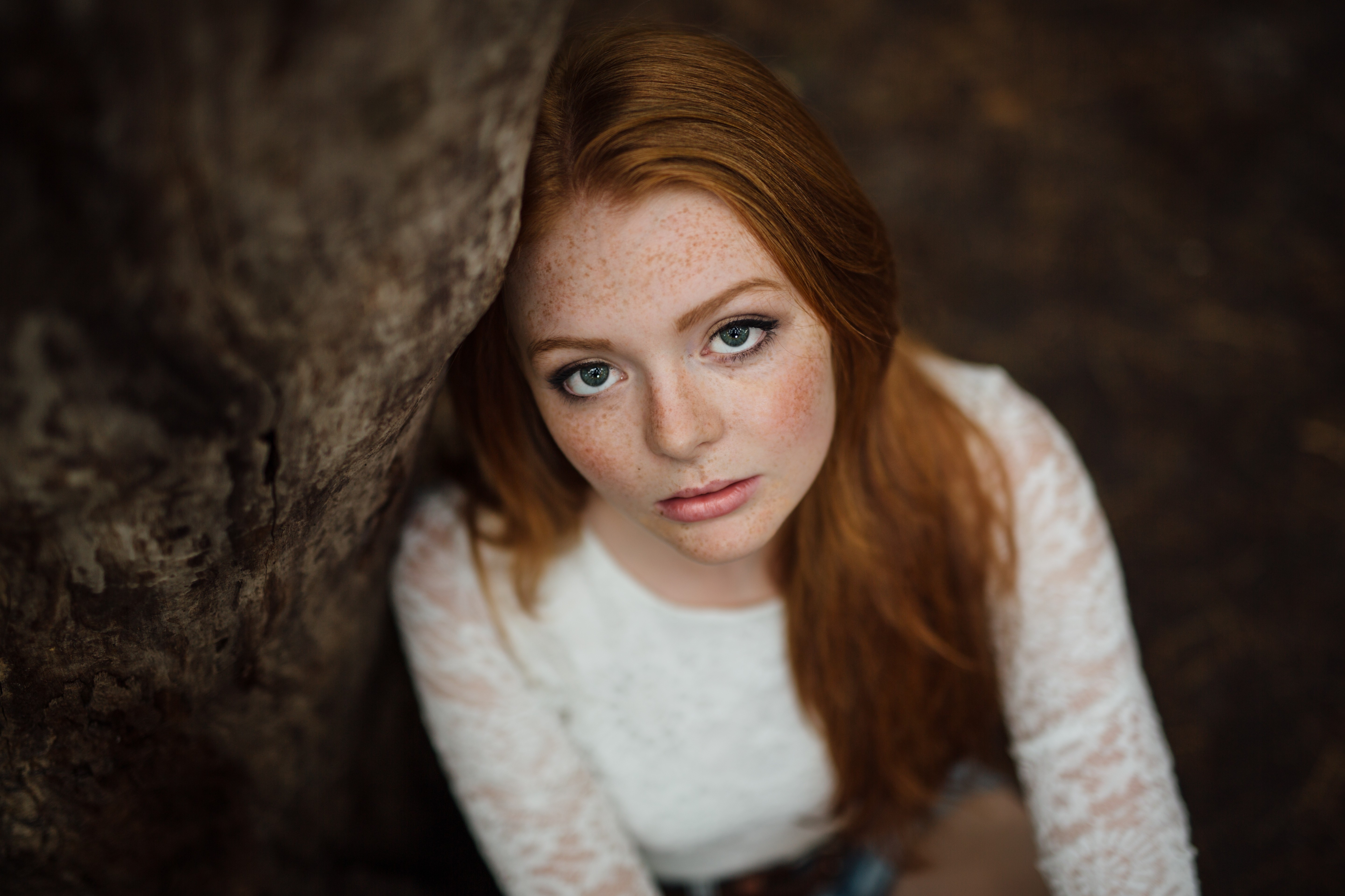 Redhead woman with freckles leaning against a tree HD Wallpaper