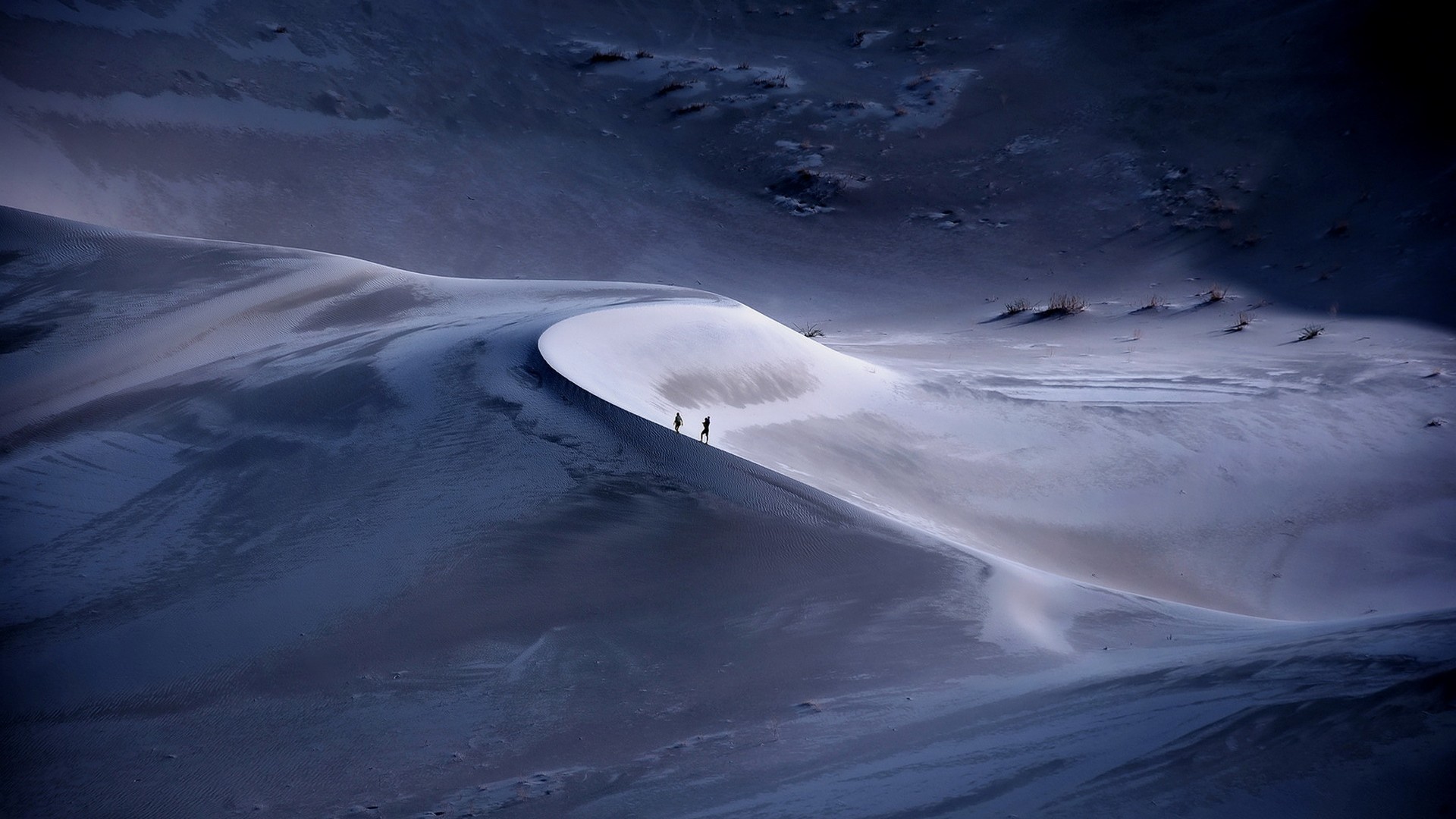 Two people walk on a sand dune in the desert HD Wallpaper
