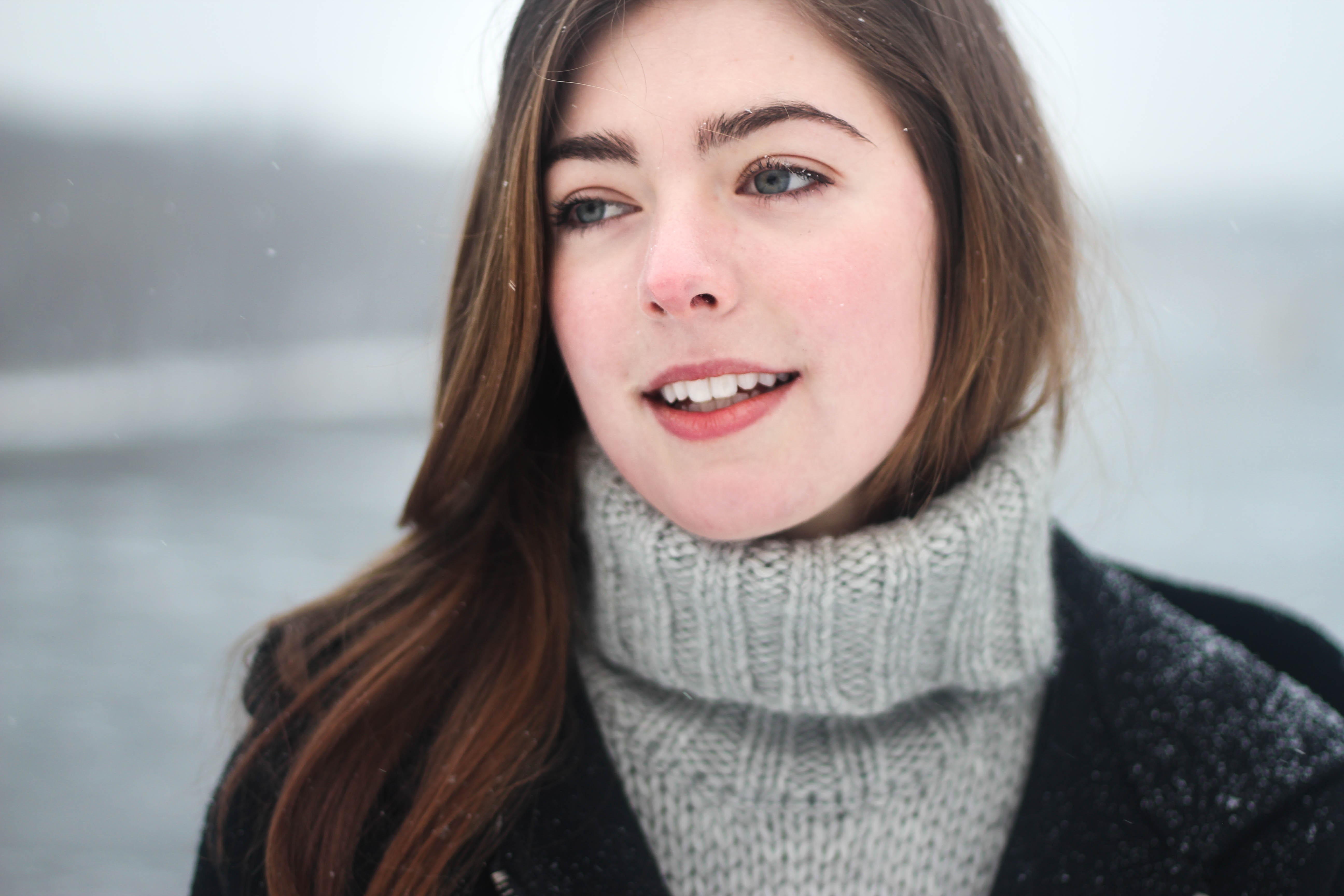 Woman in a grey turtleneck sweater and black coat outdoors in snow HD Wallpaper