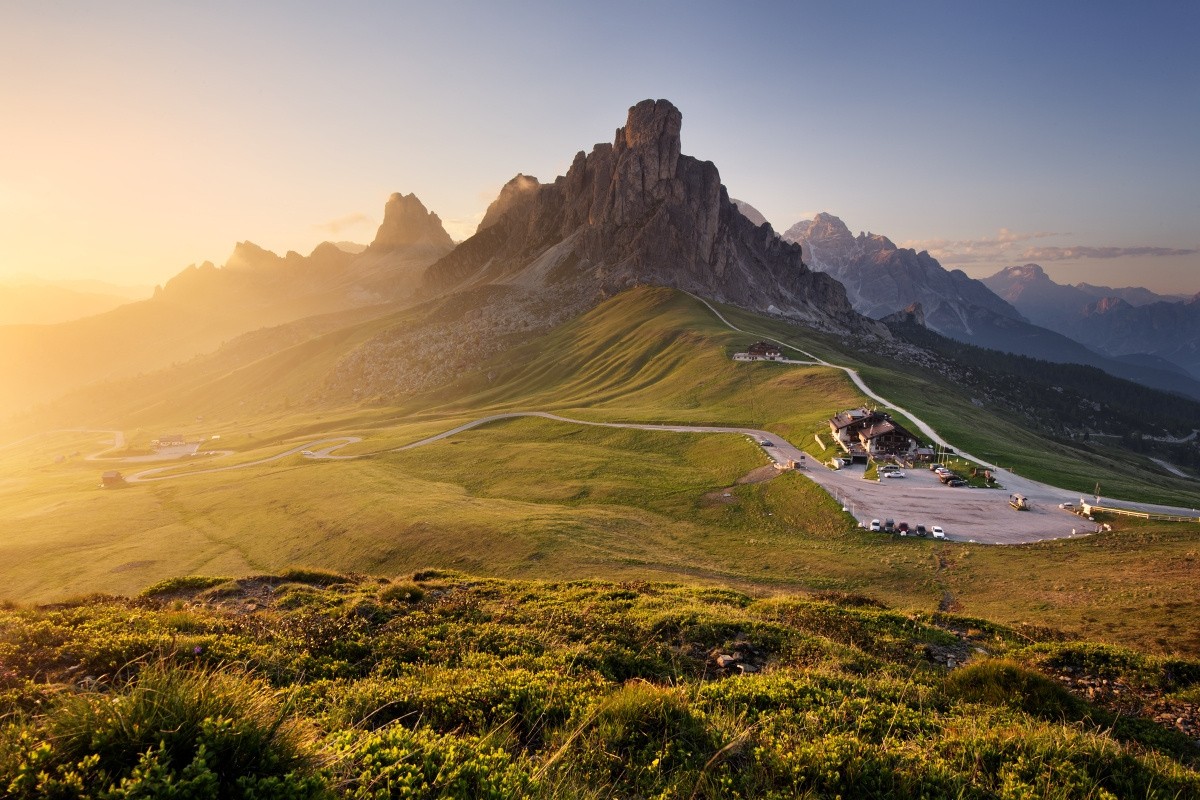 Mountain landscape with a road and buildings at sunset HD Wallpaper