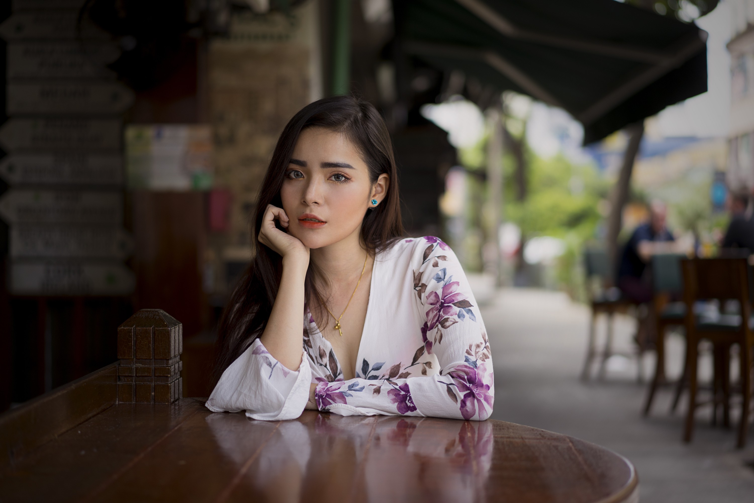 Asian woman sitting at a table in a city cafe HD Wallpaper