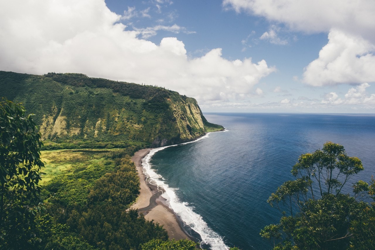 Green cliffs meet the blue ocean under a cloudy sky HD Wallpaper