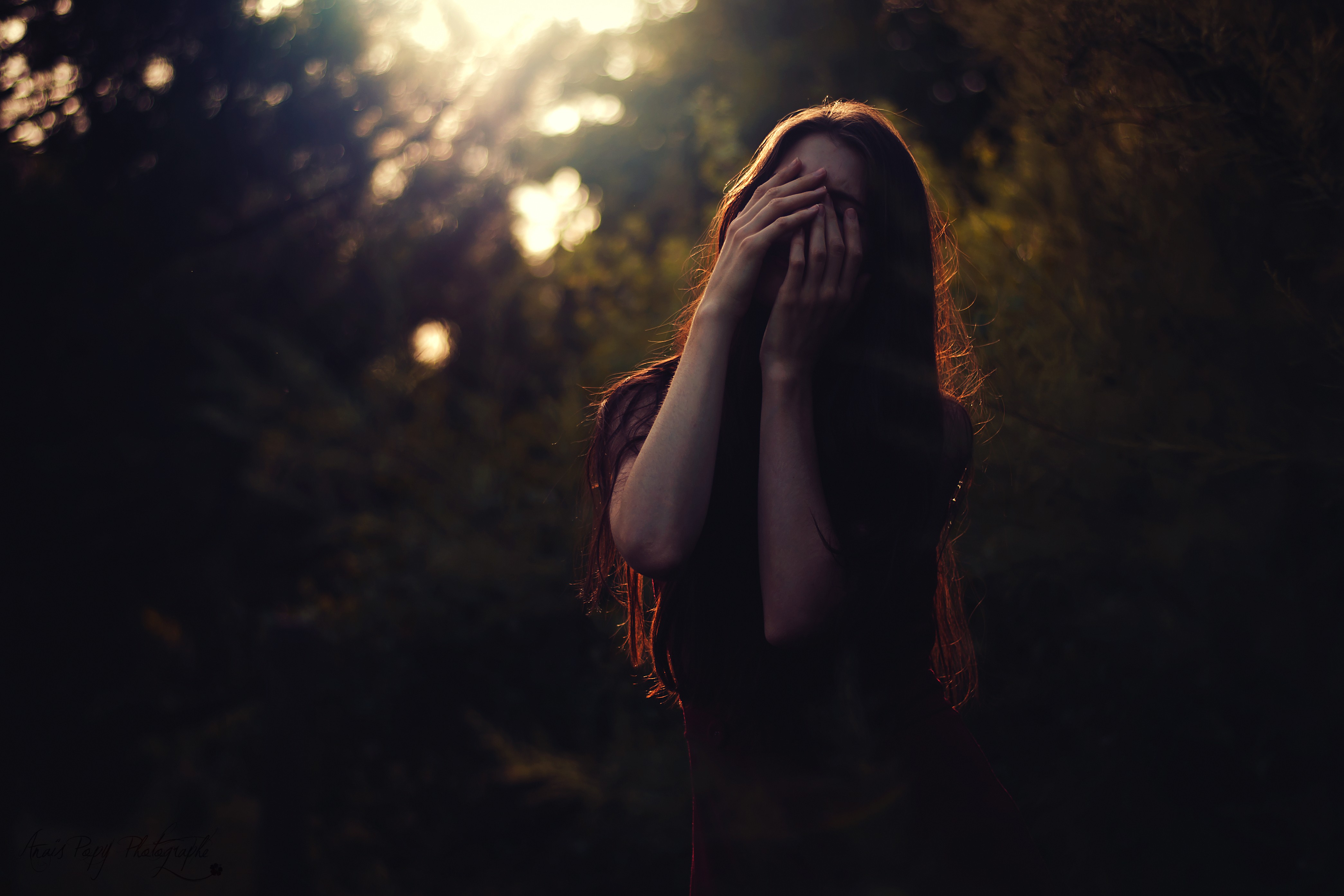 Woman with hands covering face in forest HD Wallpaper
