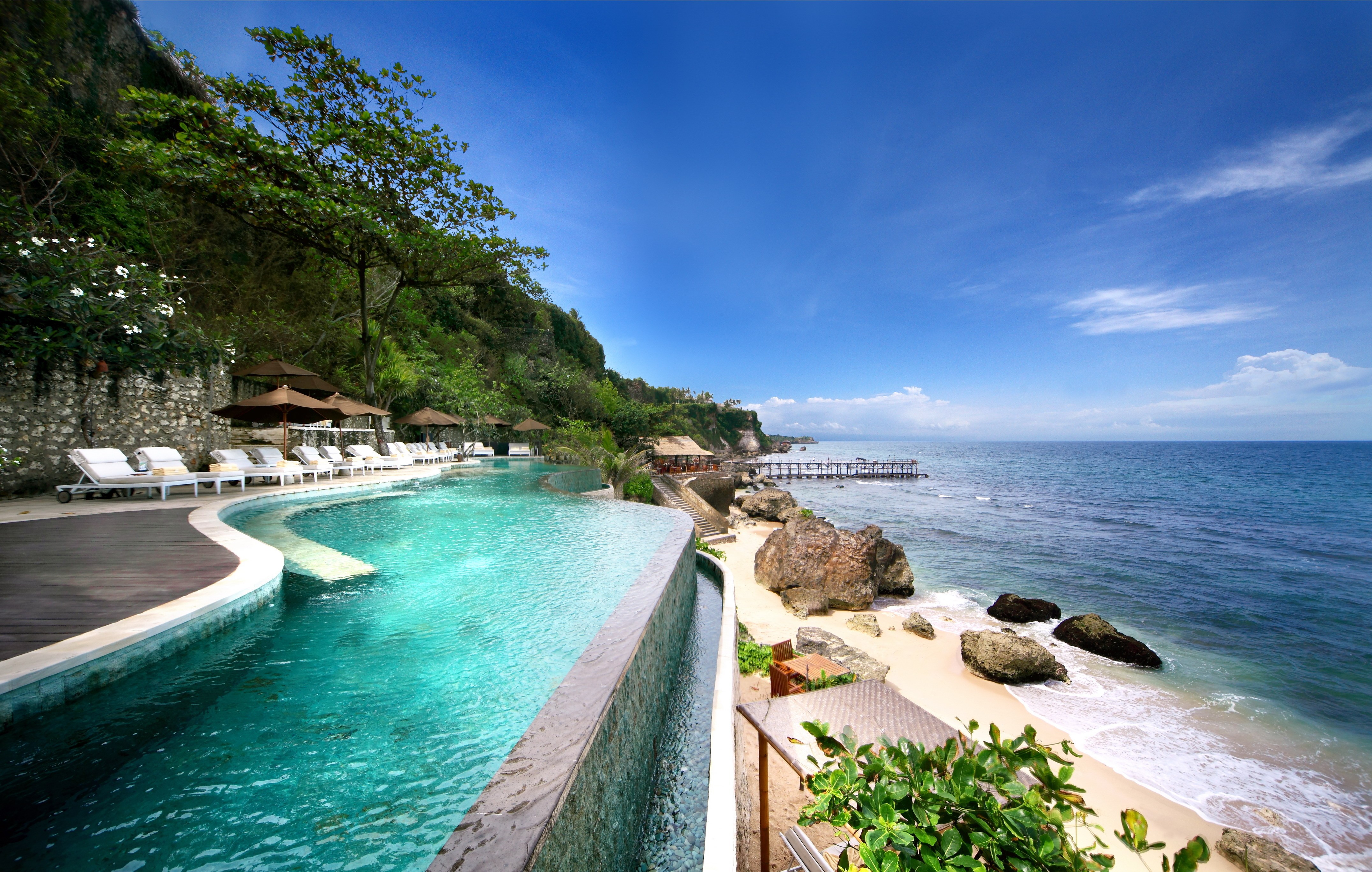 Infinity swimming pool overlooking the ocean and beach HD Wallpaper