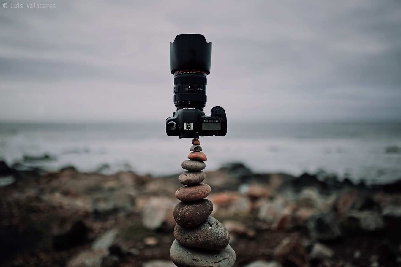 Canon camera balanced on stacked rocks by the sea HD Wallpaper
