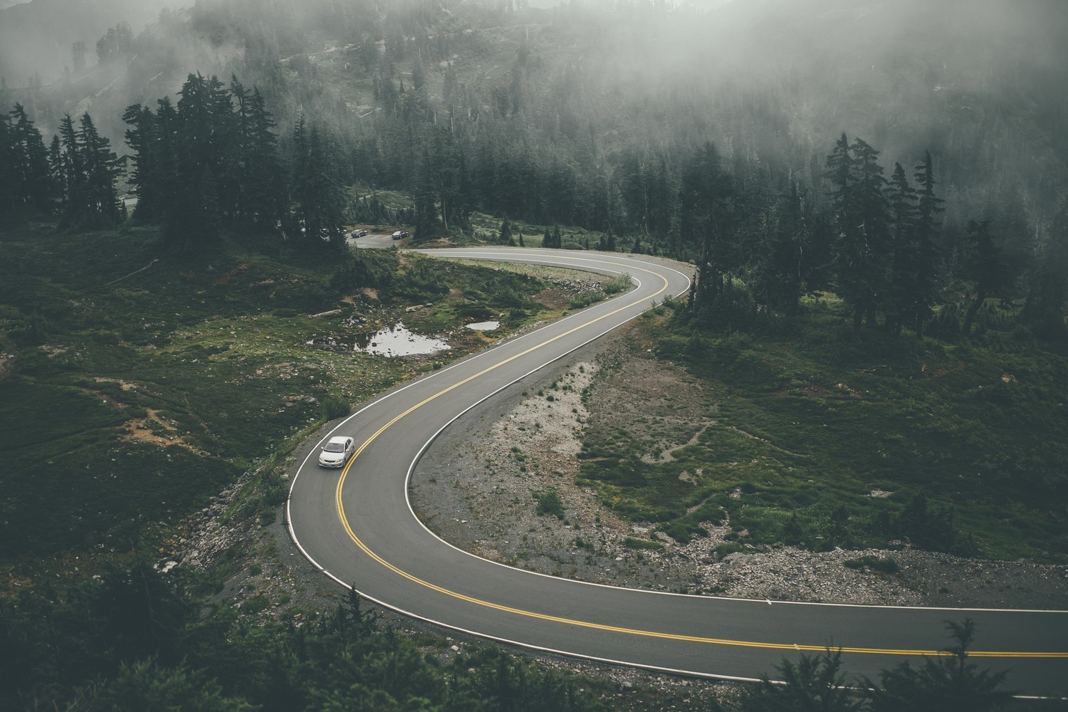 Winding mountain road through misty forest with car HD Wallpaper