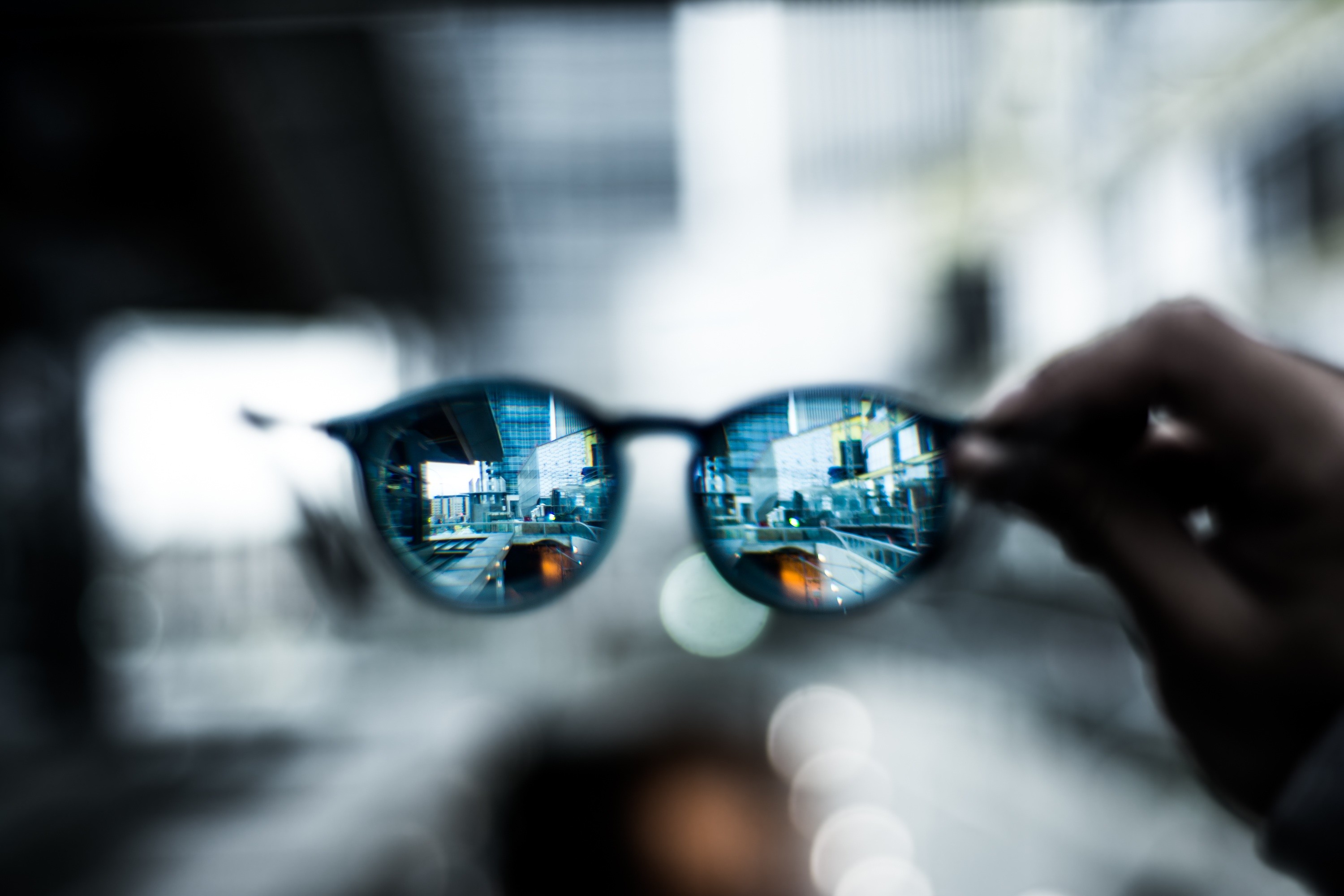 City reflected in sunglasses held by a hand HD Wallpaper