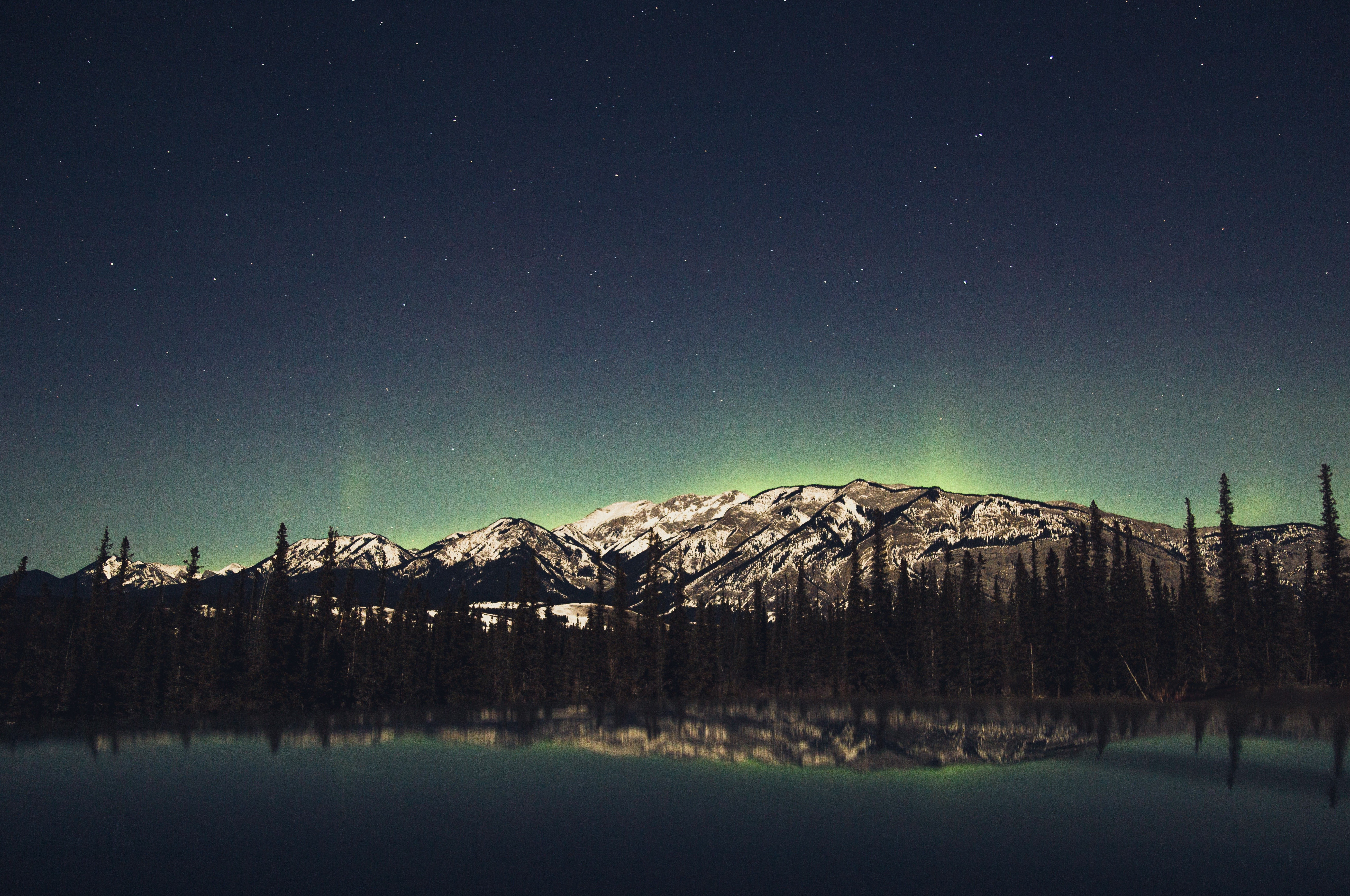 Aurora Borealis over snow-capped mountains and forest reflected in water HD Wallpaper