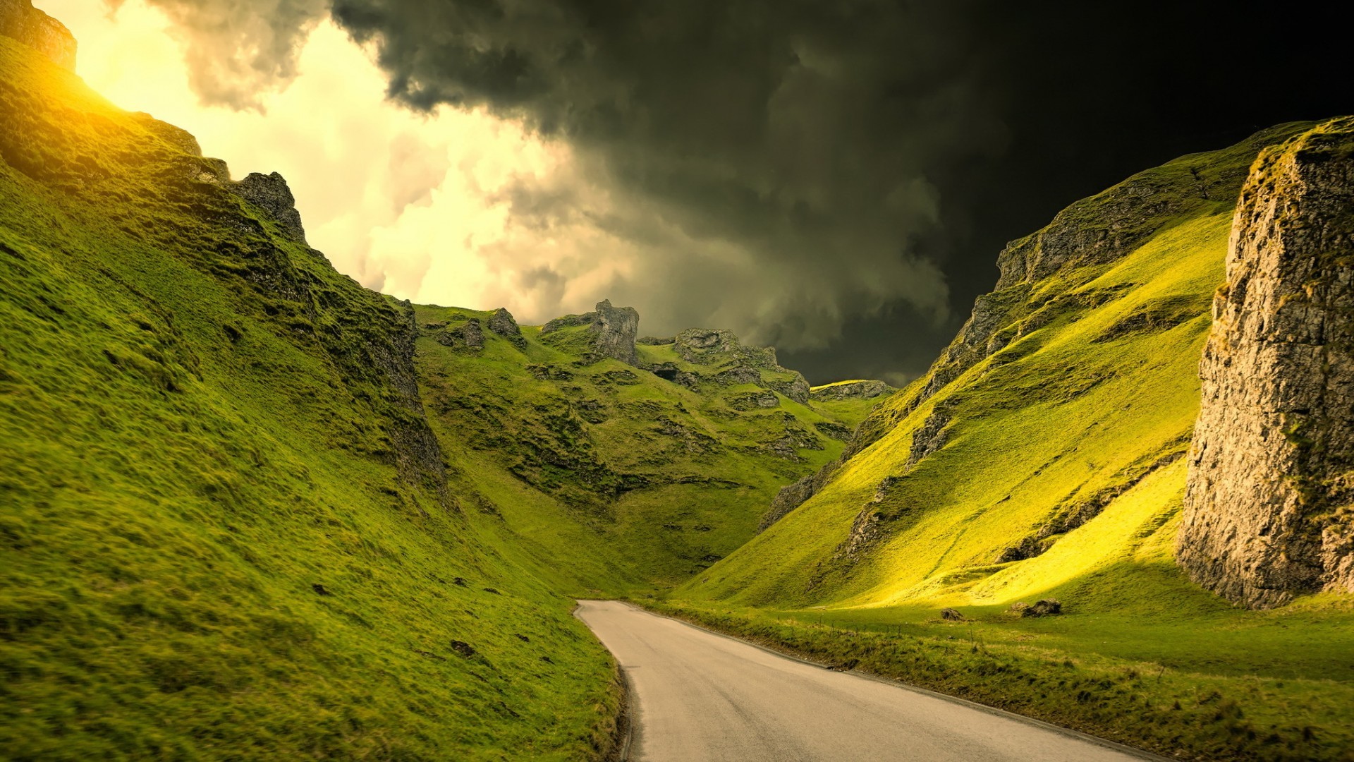 Road through a green valley under stormy skies HD Wallpaper
