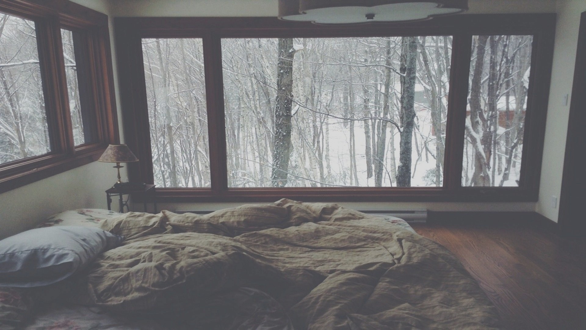 Bedroom with a large window overlooking a snowy forest HD Wallpaper