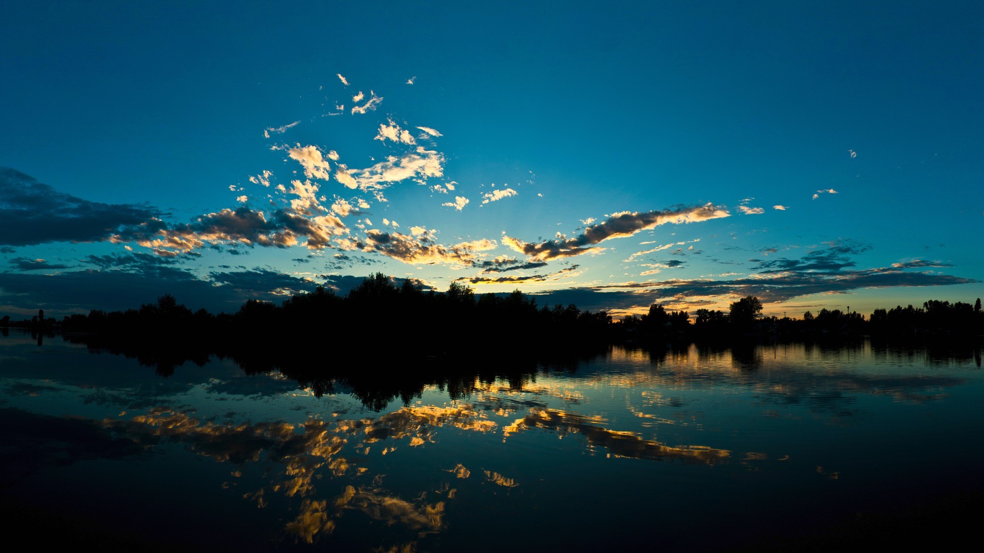 Sunset over a calm lake with silhouetted trees HD Wallpaper